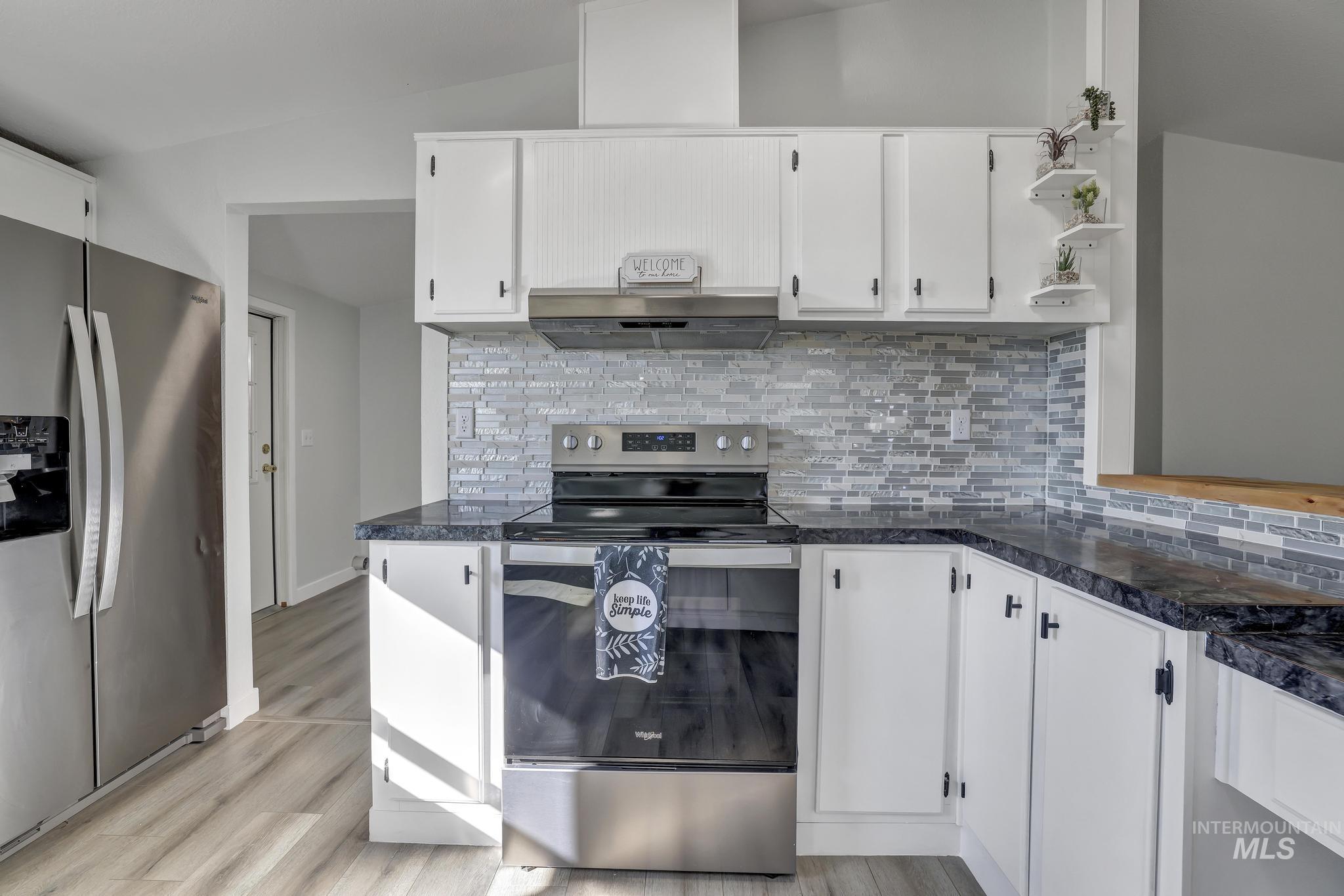 Kitchen with stainless steel appliances, decorative backsplash, white cabinets, light wood-style flooring, and lofted ceiling