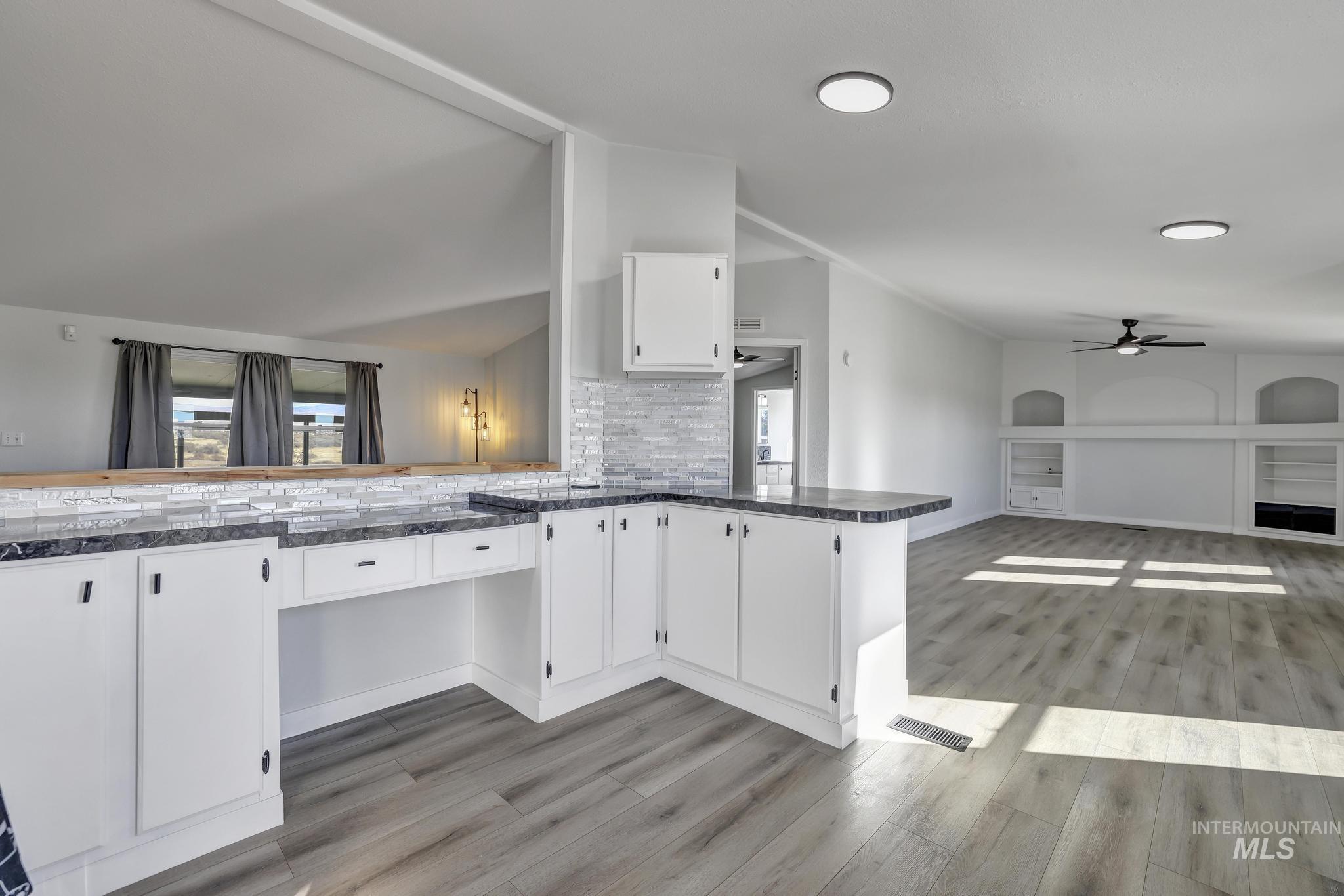 Kitchen featuring white cabinetry, a ceiling fan, dark countertops, a peninsula, and light wood-style floors