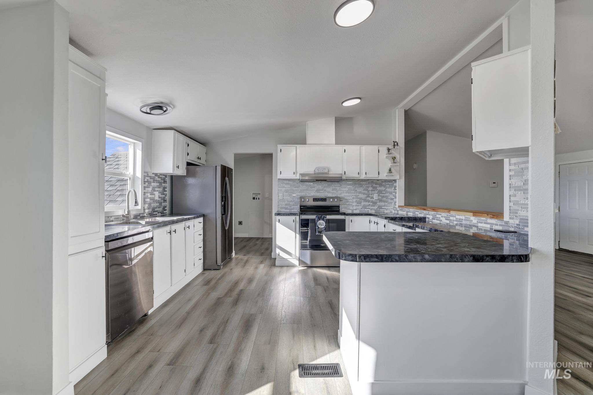 Kitchen with white cabinets, appliances with stainless steel finishes, tasteful backsplash, a peninsula, and lofted ceiling