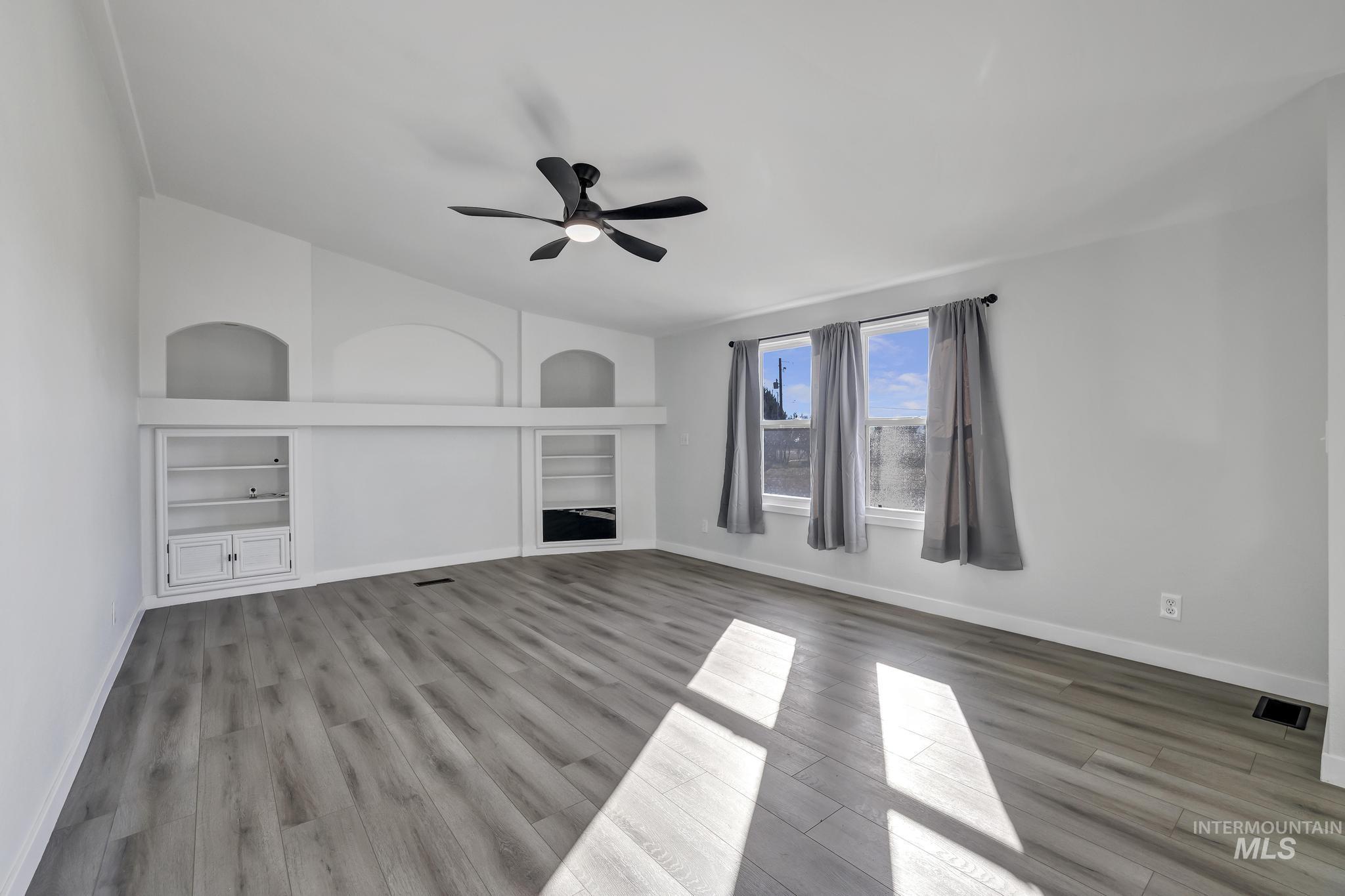Unfurnished family room featuring built in shelves, light wood finished floors, and ceiling fan