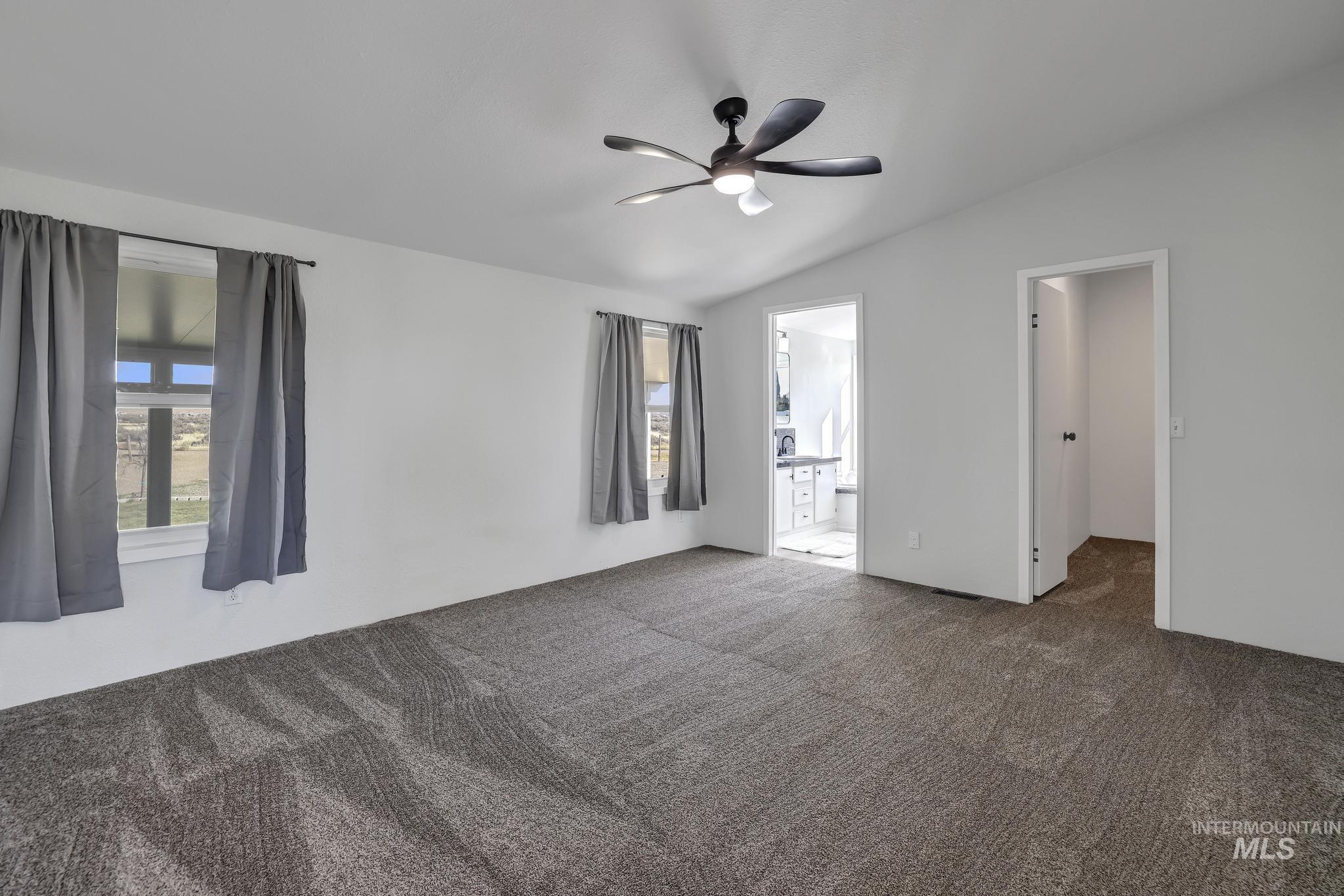 Primary bedroom with carpet flooring, vaulted ceiling, and ceiling fan
