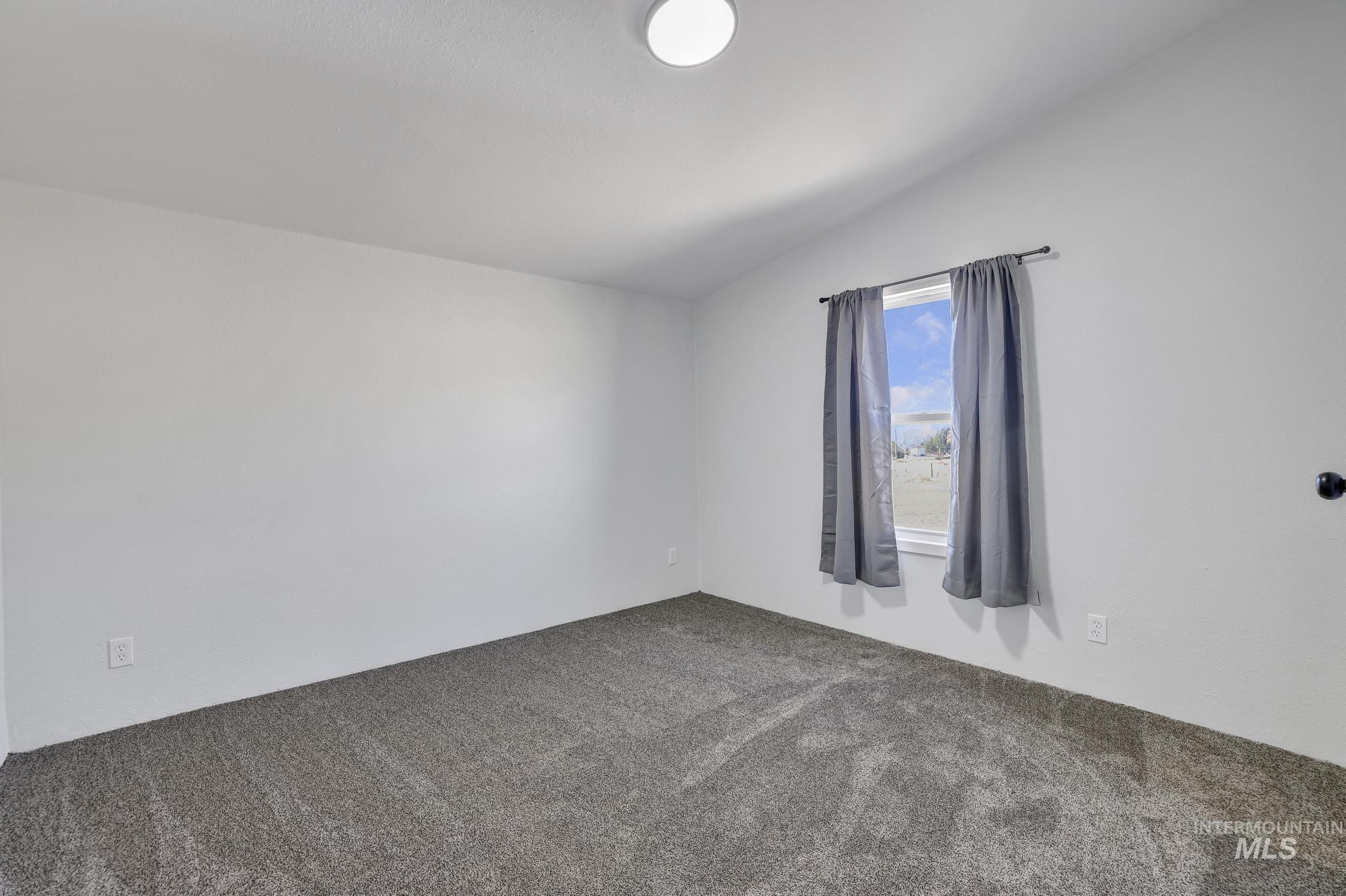 Carpeted empty room featuring vaulted ceiling