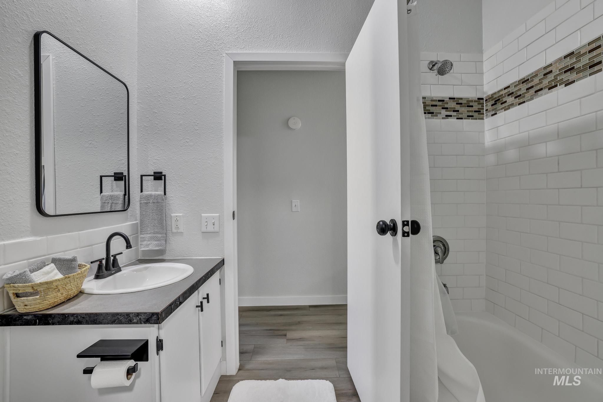 Bathroom with vanity, shower / bathtub combination with curtain, light wood-style flooring, and a textured wall