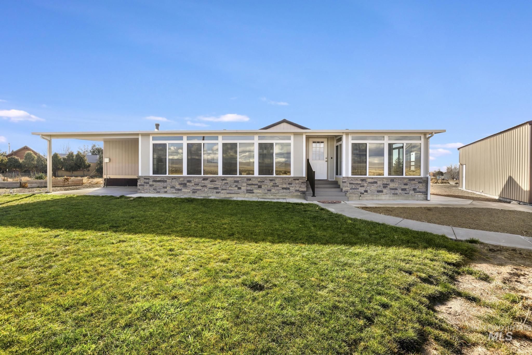 View of front facade with a front yard, entry steps, a sunroom, and stone siding