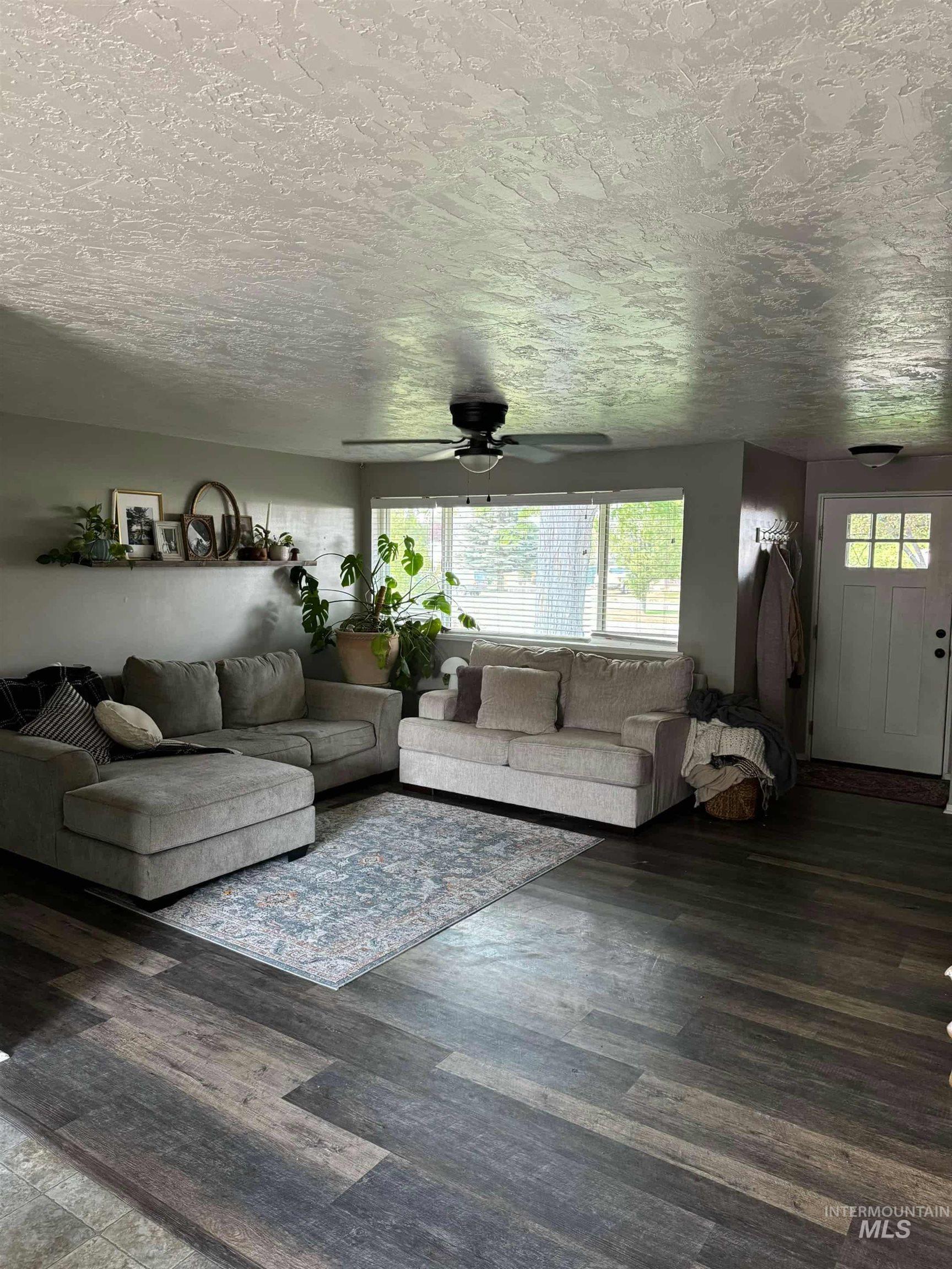 Living room featuring a textured ceiling, wood finished floors, and a ceiling fan