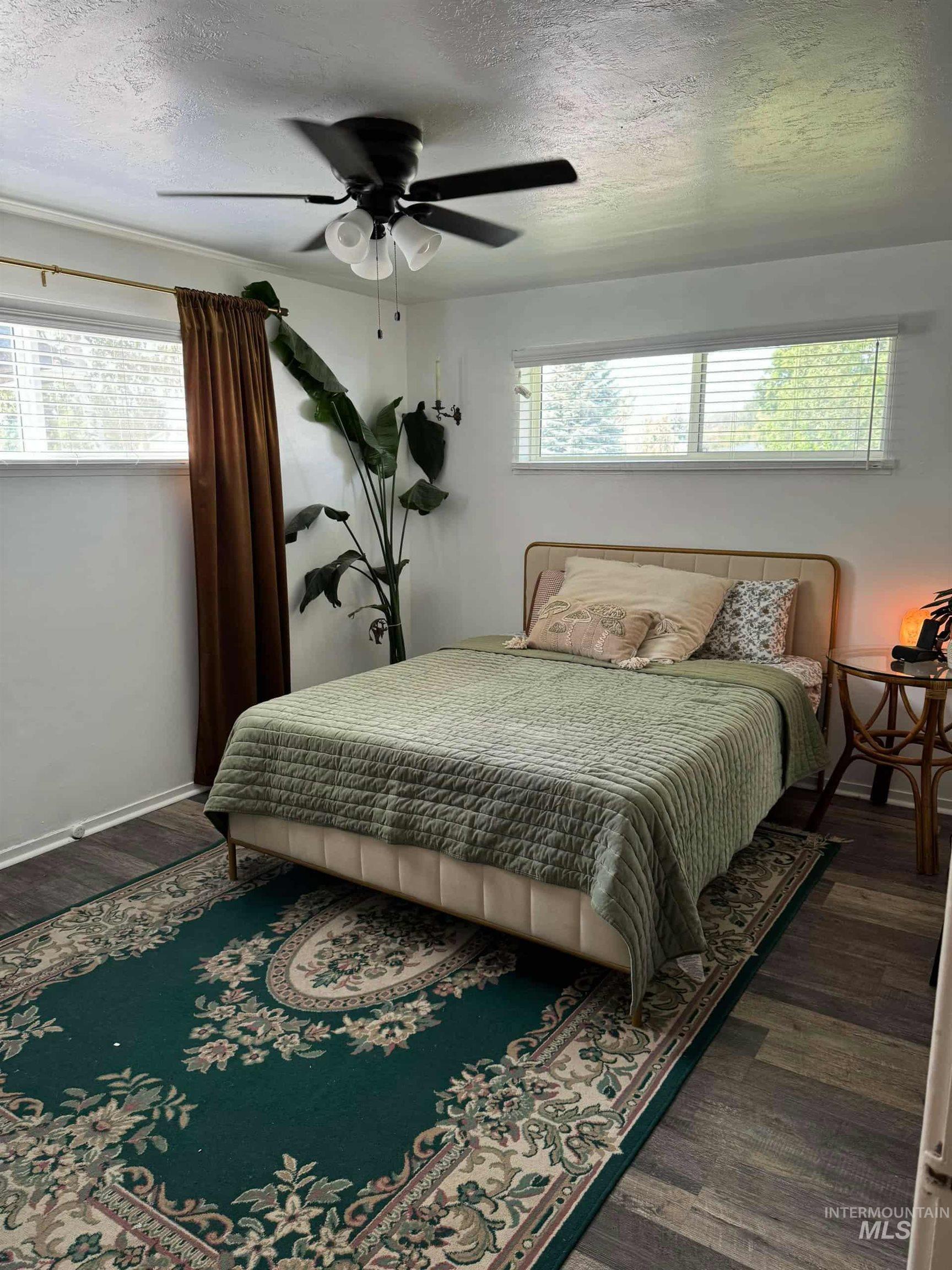 Bedroom with a textured ceiling, multiple windows, a ceiling fan, and dark wood-style flooring