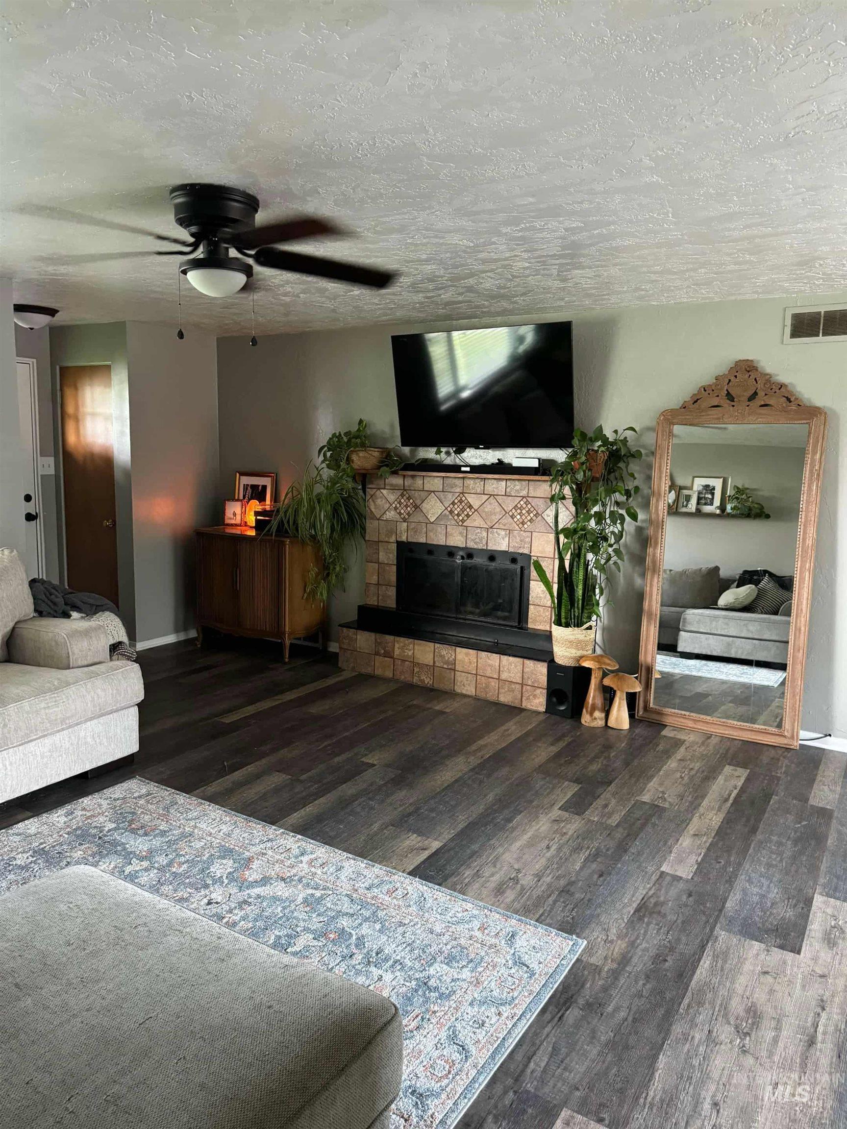 Living room with a textured ceiling, wood finished floors, a tile fireplace, and ceiling fan