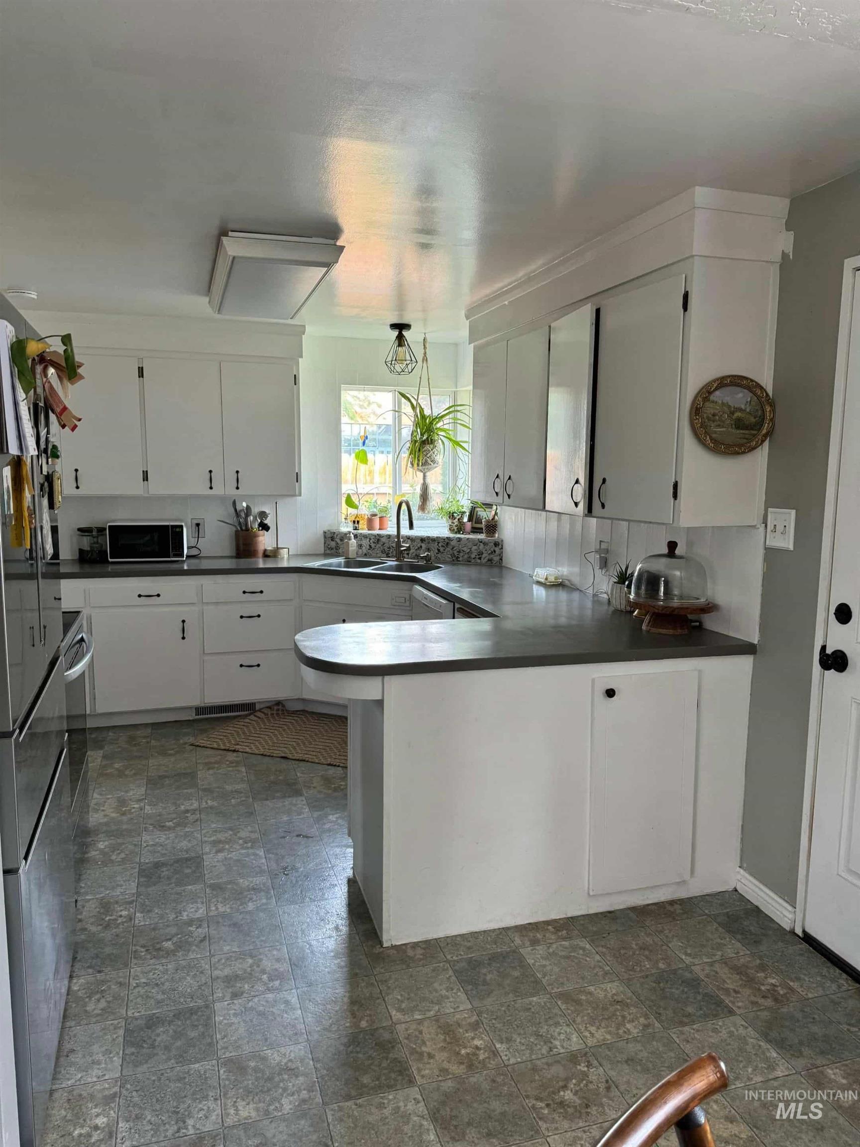 Kitchen with a peninsula, white cabinets, dark countertops, stone finish floors, and freestanding refrigerator