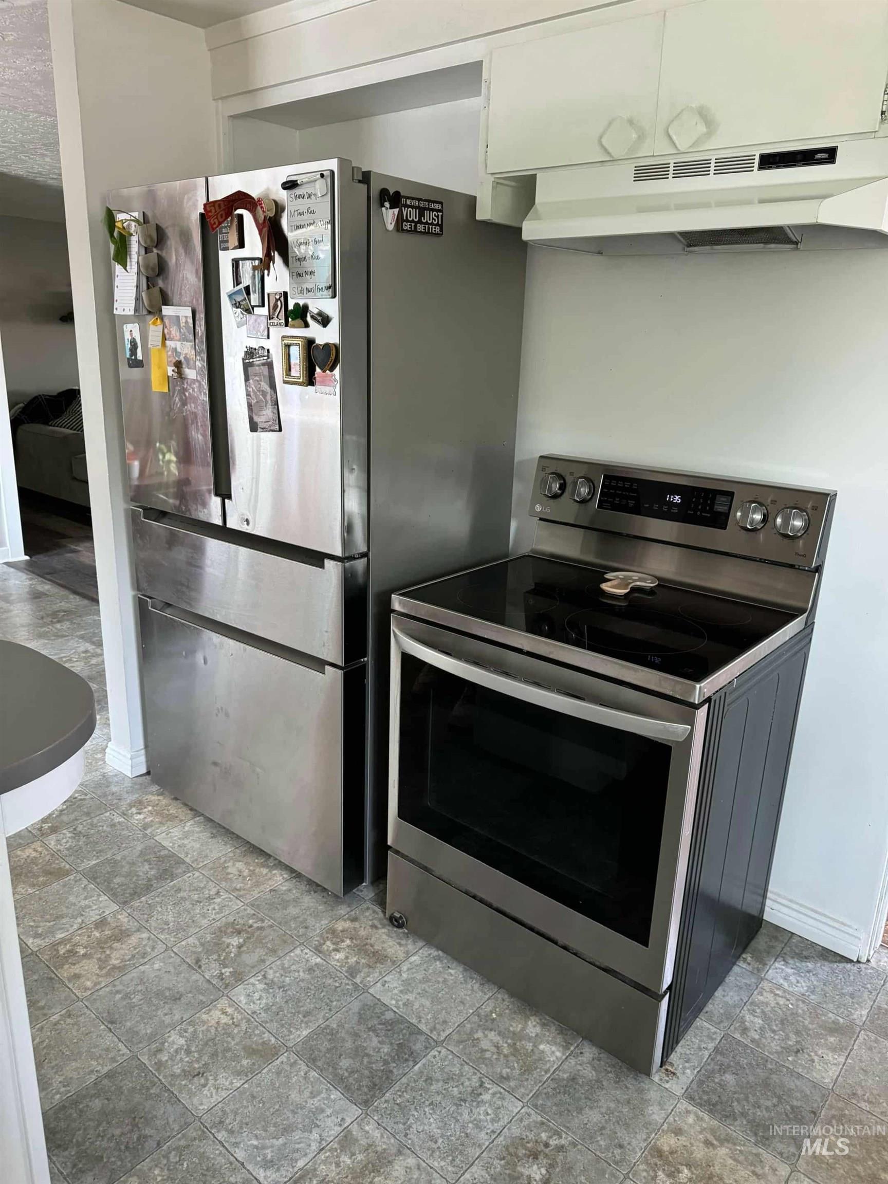 Kitchen featuring appliances with stainless steel finishes, under cabinet range hood, white cabinets, and light stone finish flooring