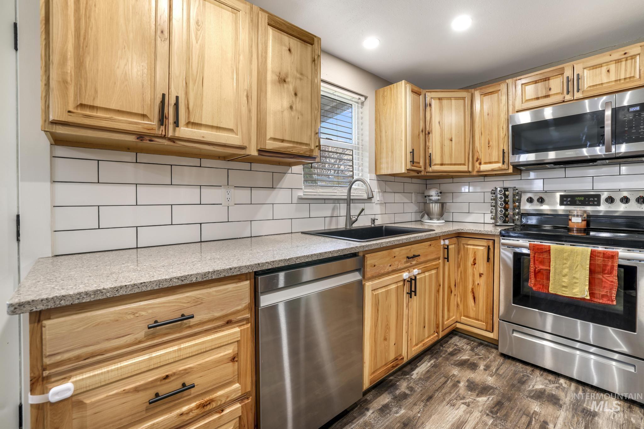 Kitchen with stainless steel appliances, tasteful backsplash, light stone counters, dark wood-type flooring, and recessed lighting