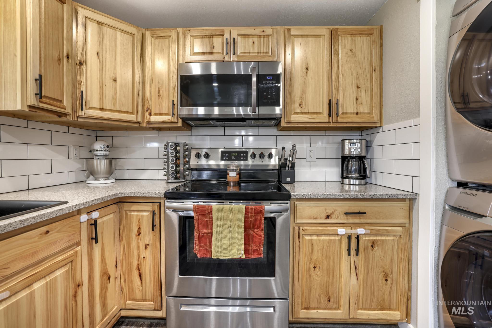 Kitchen featuring appliances with stainless steel finishes, stacked washer / drying machine, light stone counters, and tasteful backsplash