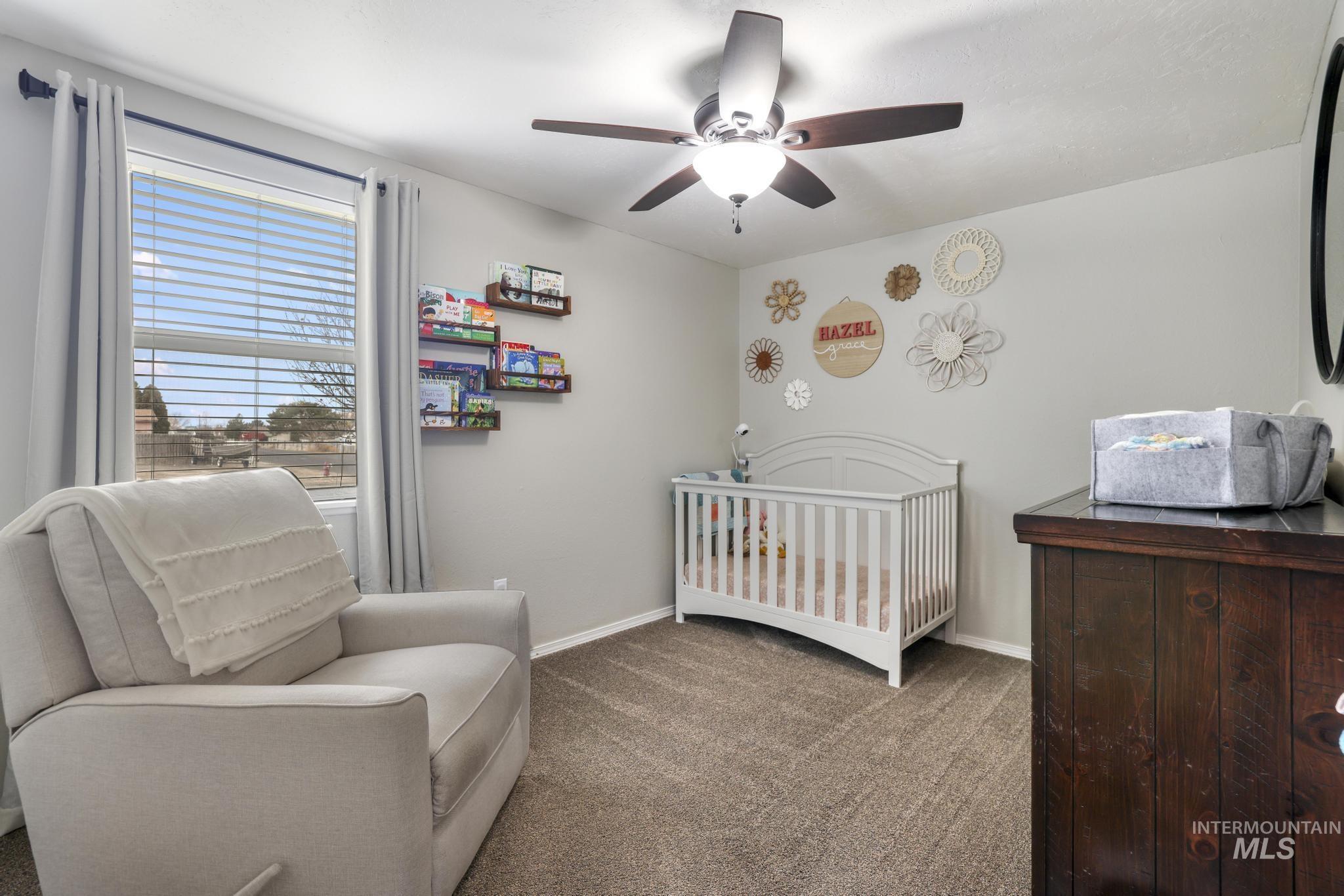 Carpeted bedroom featuring a crib and a ceiling fan