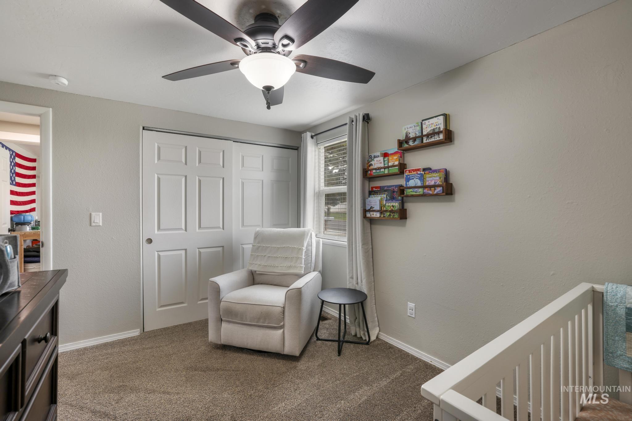 Living area with carpet flooring, a ceiling fan, and a textured wall