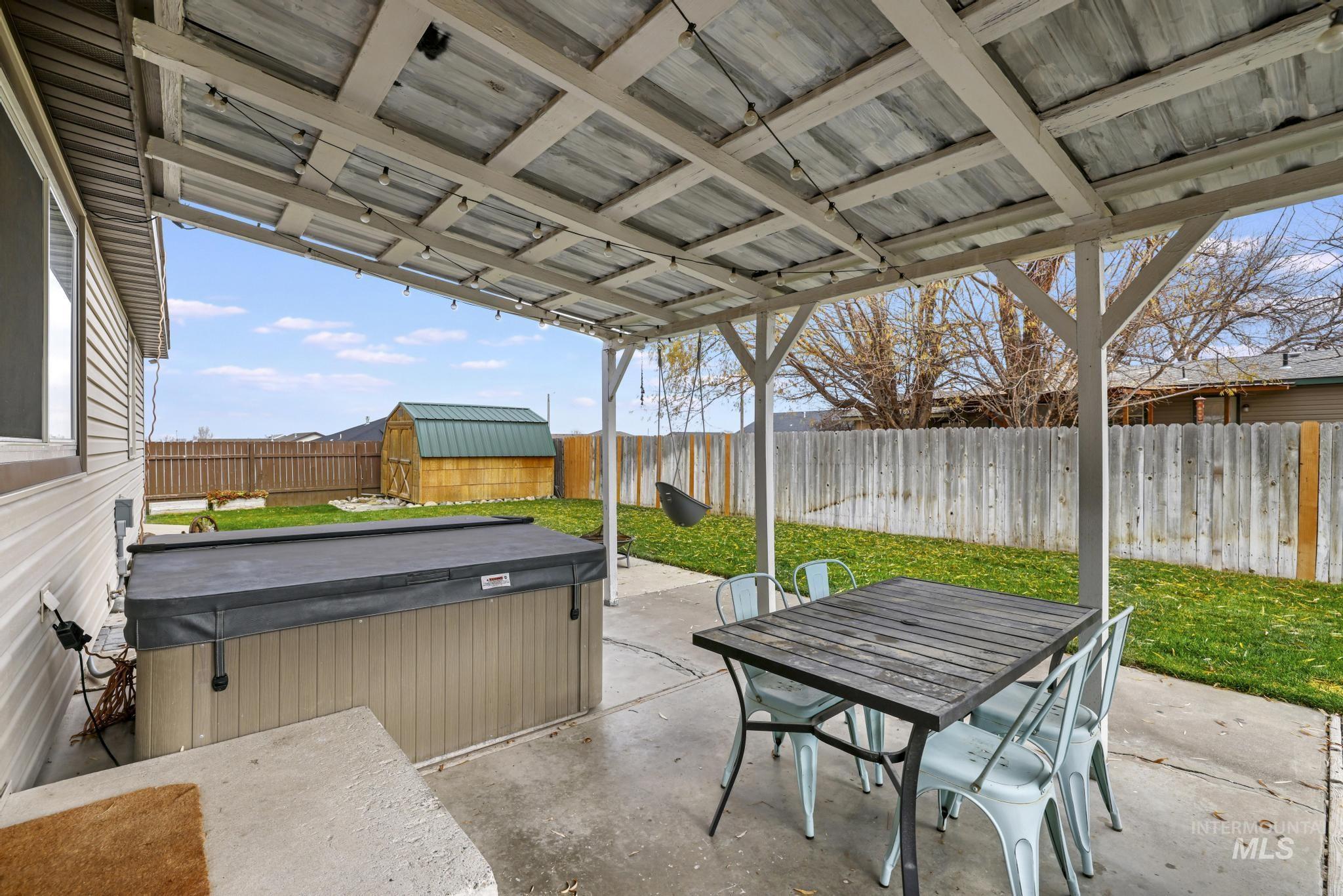 Fenced backyard featuring a hot tub, a patio area, outdoor dining space, and a storage unit
