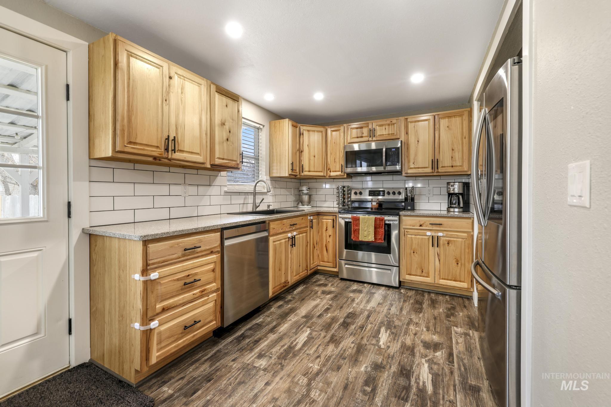 Kitchen featuring appliances with stainless steel finishes, tasteful backsplash, dark wood-style floors, recessed lighting, and light stone counters