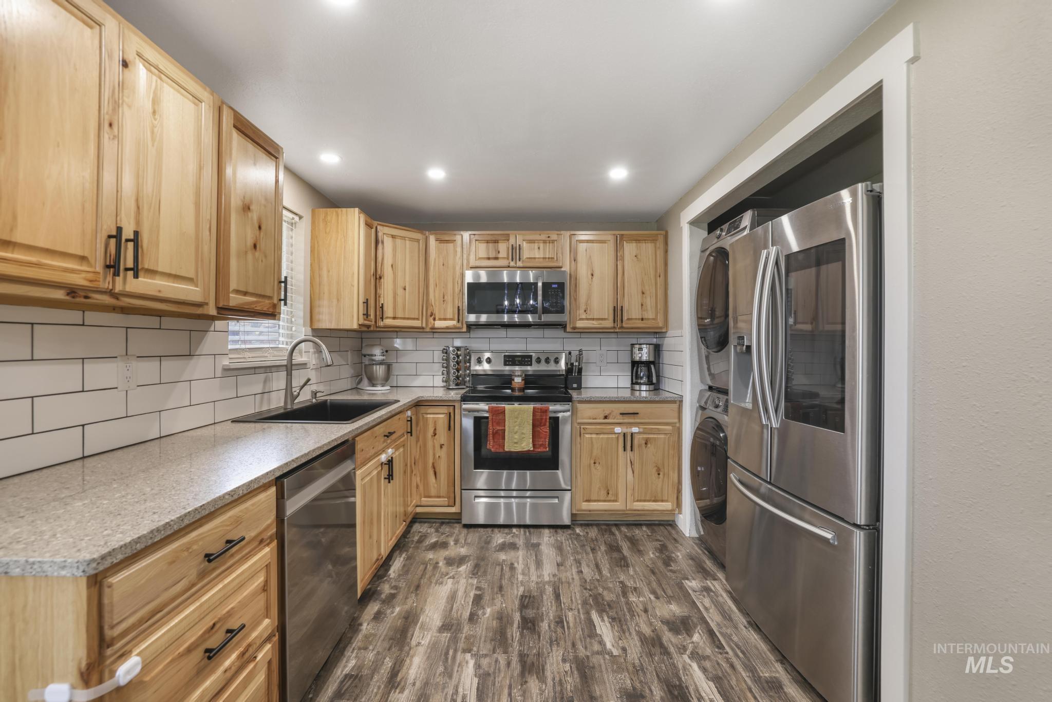 Kitchen with appliances with stainless steel finishes, tasteful backsplash, dark wood-style floors, recessed lighting, and washer / clothes dryer