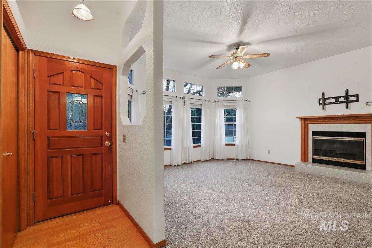 Foyer entrance featuring a glass covered fireplace, a textured ceiling, light carpet, a ceiling fan, and light wood-style floors