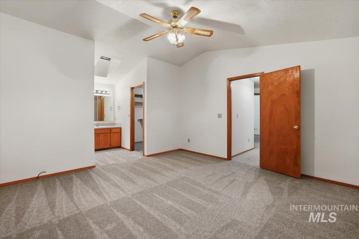 Unfurnished bedroom featuring lofted ceiling, a spacious closet, light colored carpet, a ceiling fan, and a textured ceiling