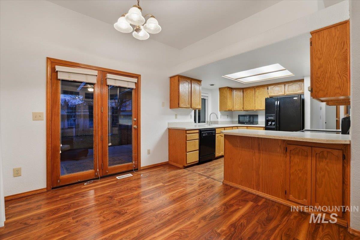 Kitchen with dark wood finished floors, black appliances, light countertops, pendant lighting, and brown cabinets
