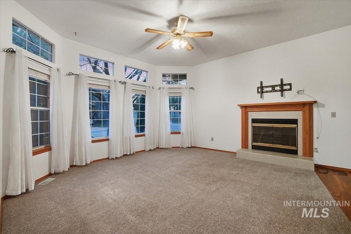 Unfurnished living room featuring a glass covered fireplace, carpet floors, a textured ceiling, and ceiling fan