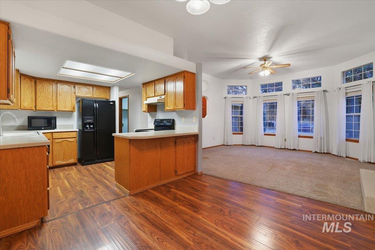 Kitchen with light countertops, brown cabinets, black appliances, and a peninsula