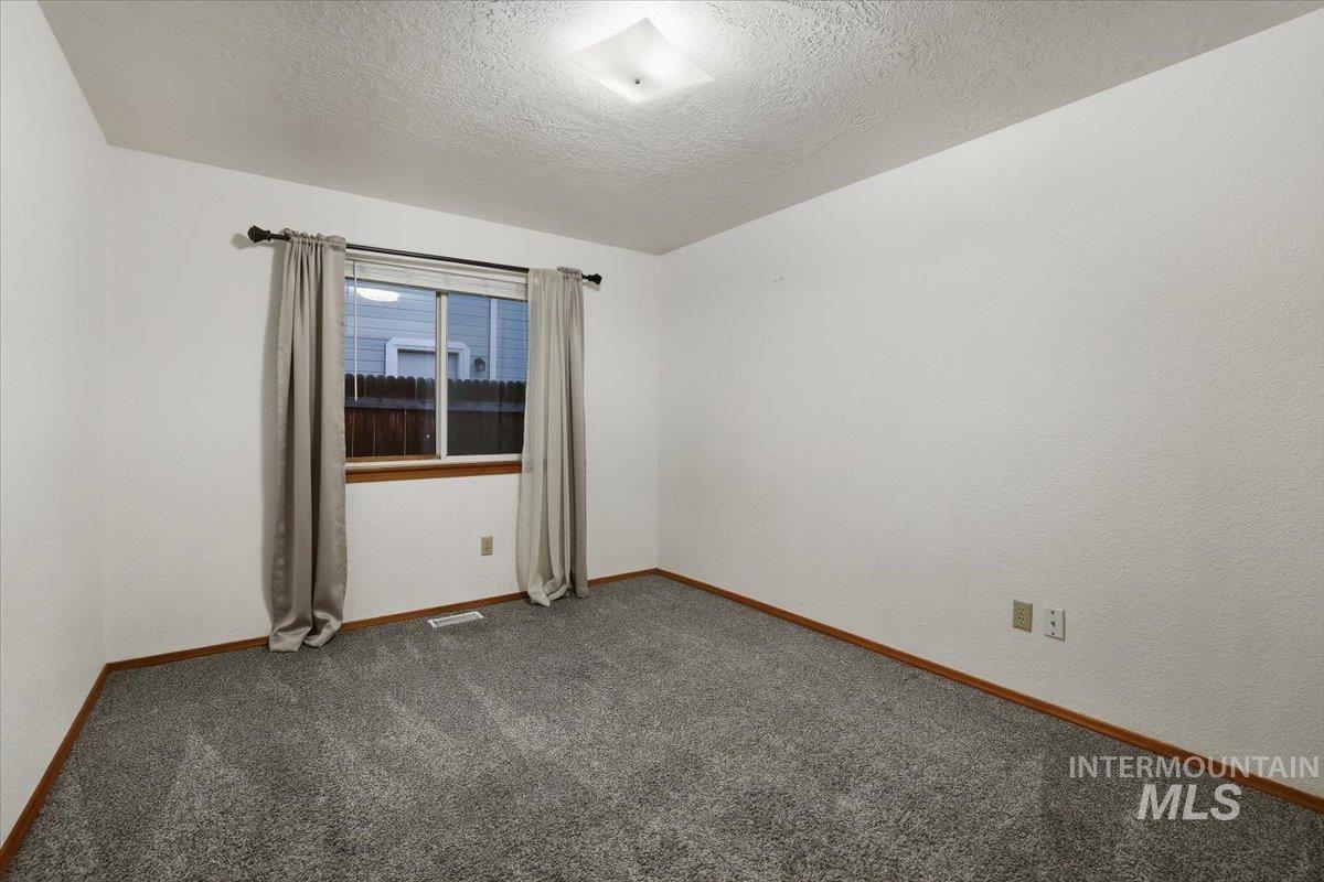 Carpeted spare room featuring a textured ceiling and a textured wall