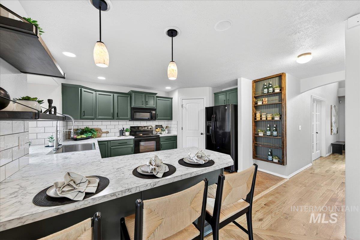 Kitchen featuring green cabinets, tasteful backsplash, a peninsula, light wood-style flooring, and light countertops