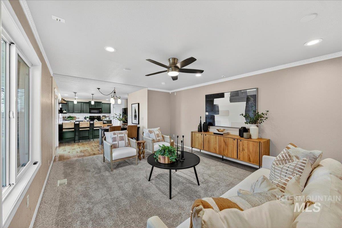 Living room with crown molding, recessed lighting, a ceiling fan, light carpet, and a chandelier