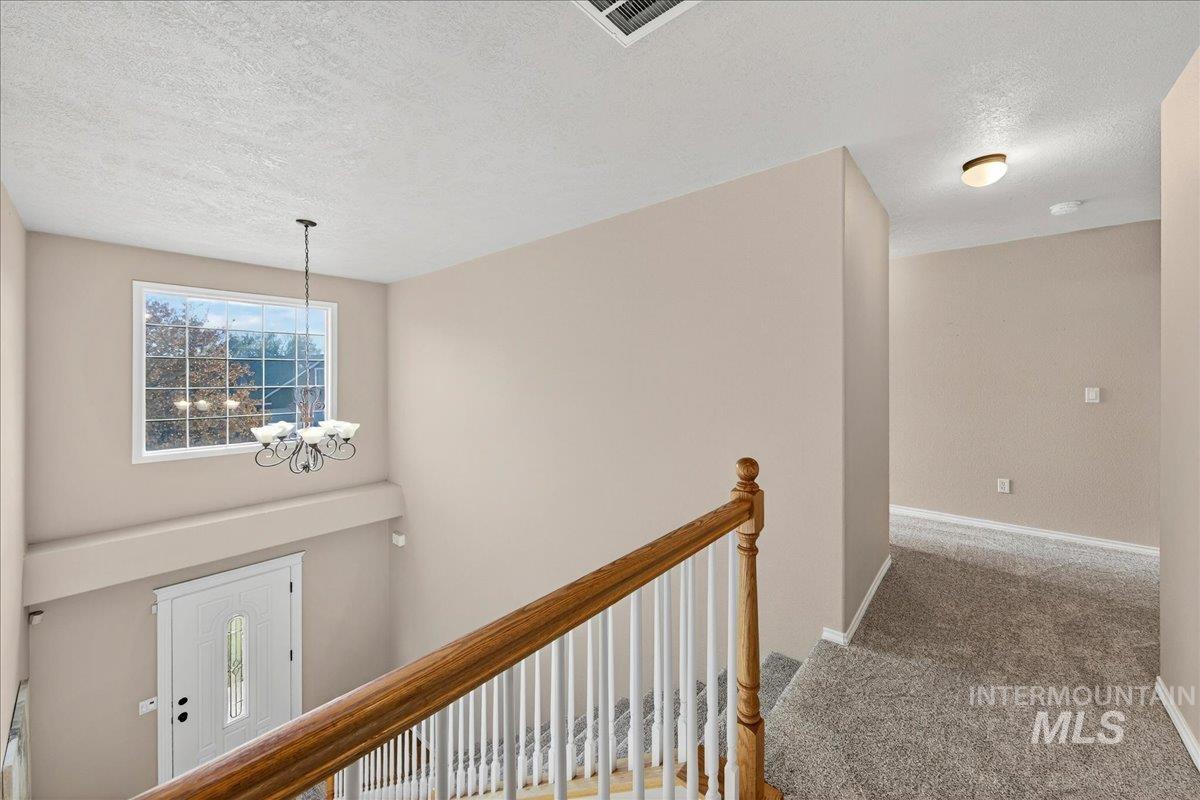 Hall featuring a textured ceiling, light colored carpet, a chandelier, and an upstairs landing
