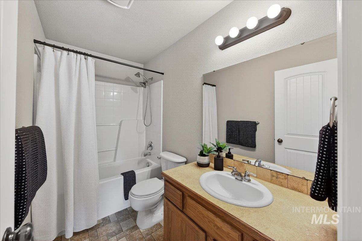 Full bathroom featuring shower / tub combo with curtain, vanity, and stone finish flooring