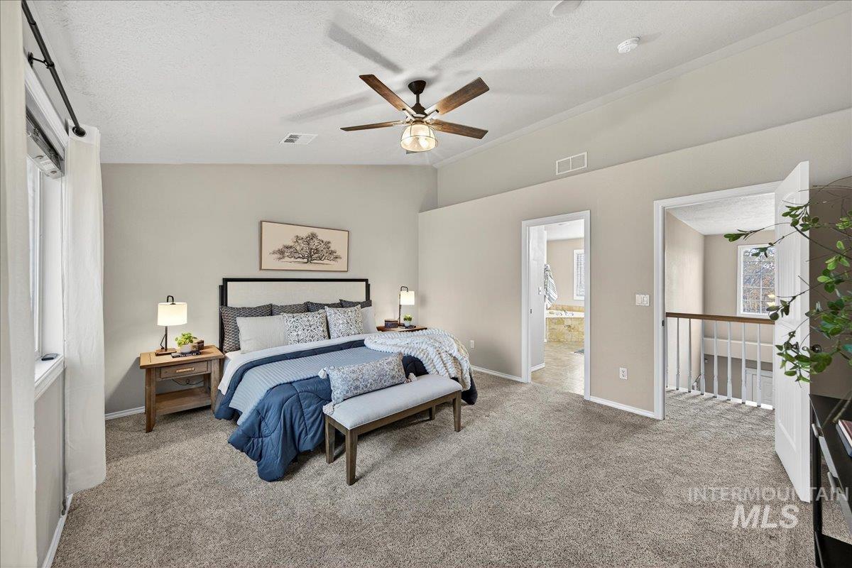 Bedroom with vaulted ceiling, a textured ceiling, light carpet, ceiling fan, and ensuite bathroom