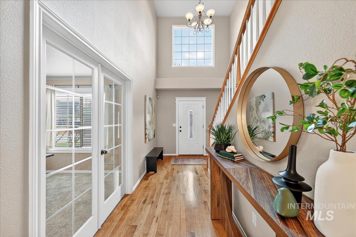 Entrance foyer featuring light wood-style floors, a towering ceiling, a textured wall, a chandelier, and french doors