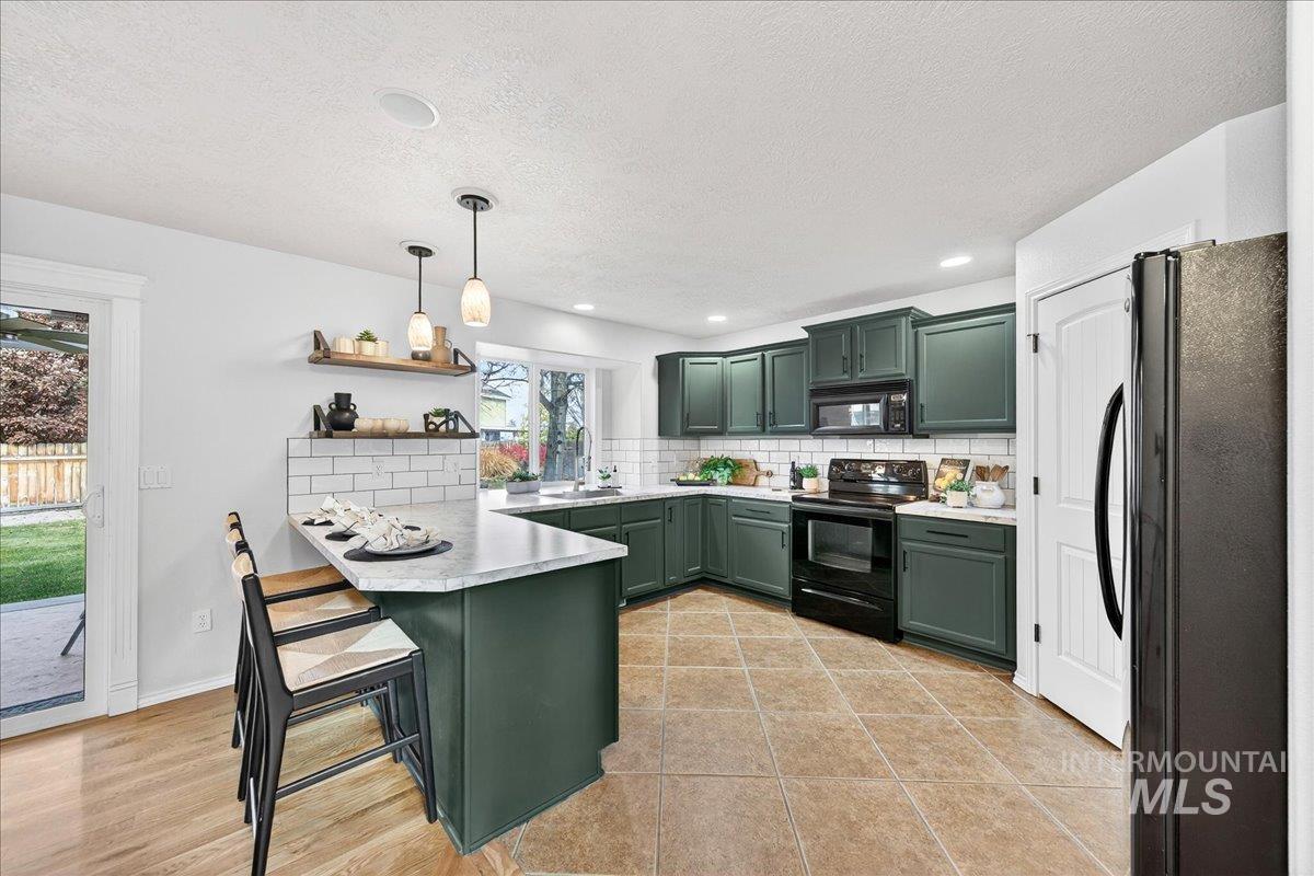 Kitchen featuring green cabinetry, black appliances, decorative backsplash, a peninsula, and a breakfast bar