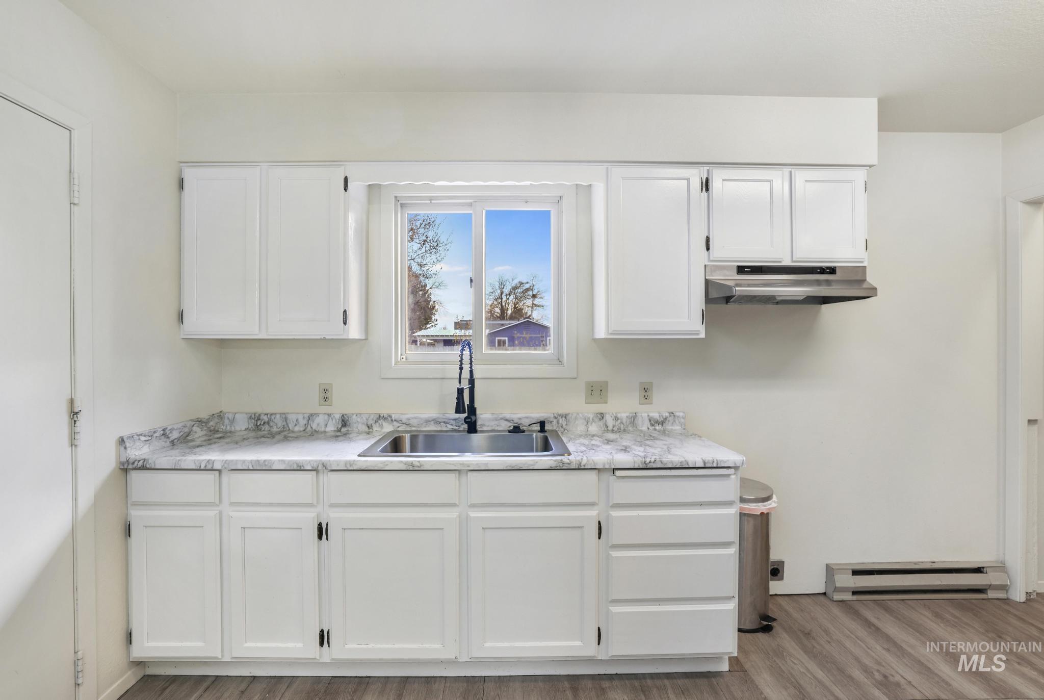 Kitchen featuring white cabinetry, light countertops, light wood-type flooring, a baseboard radiator, and under cabinet range hood