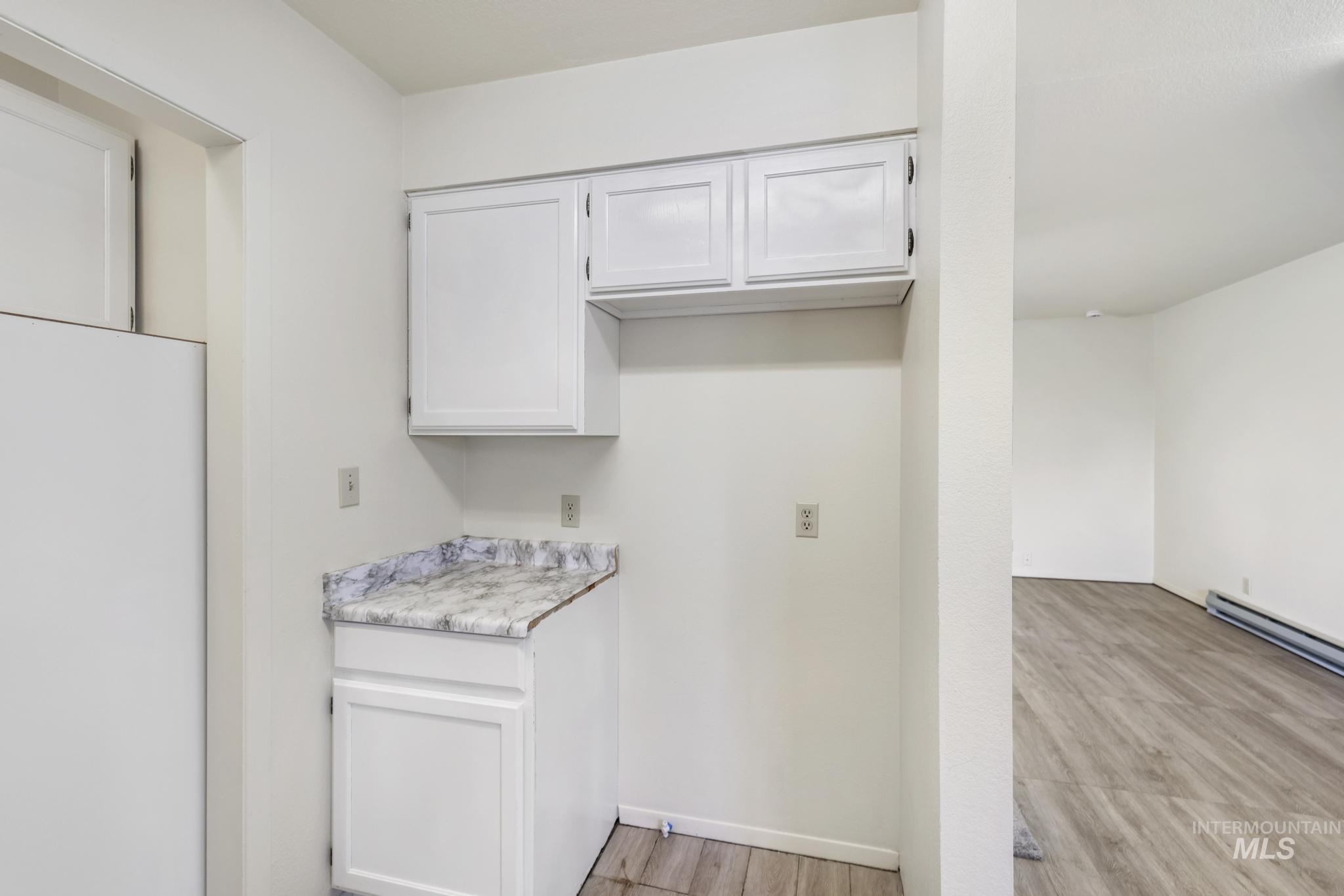 Kitchen featuring white cabinets, light countertops, freestanding refrigerator, and light wood-type flooring