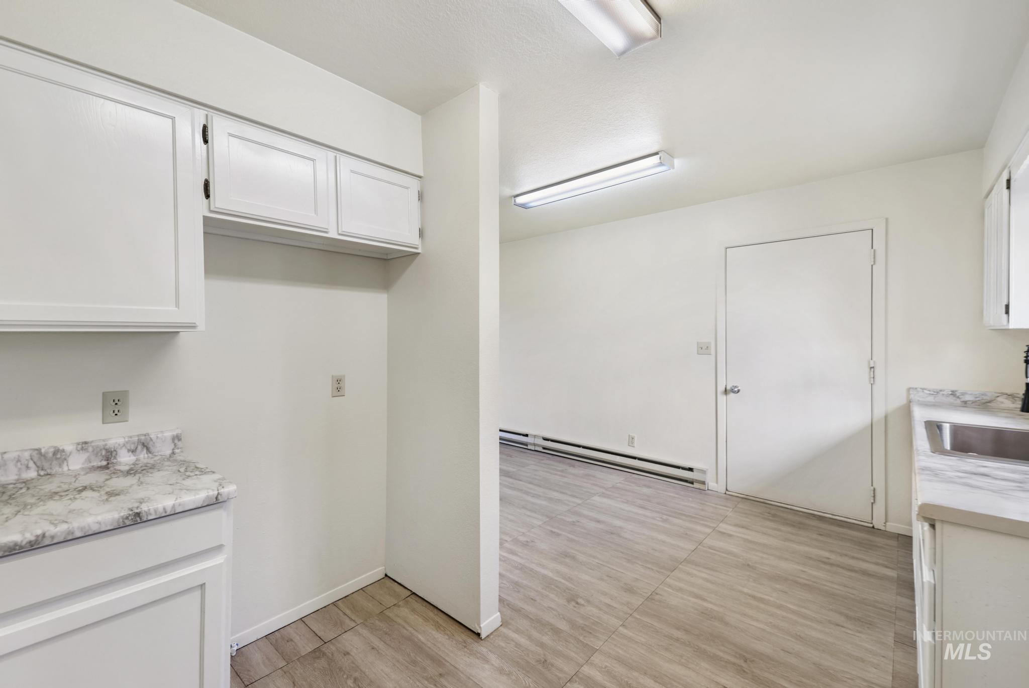 Kitchen with light countertops, white cabinets, a baseboard radiator, and light wood-style floors