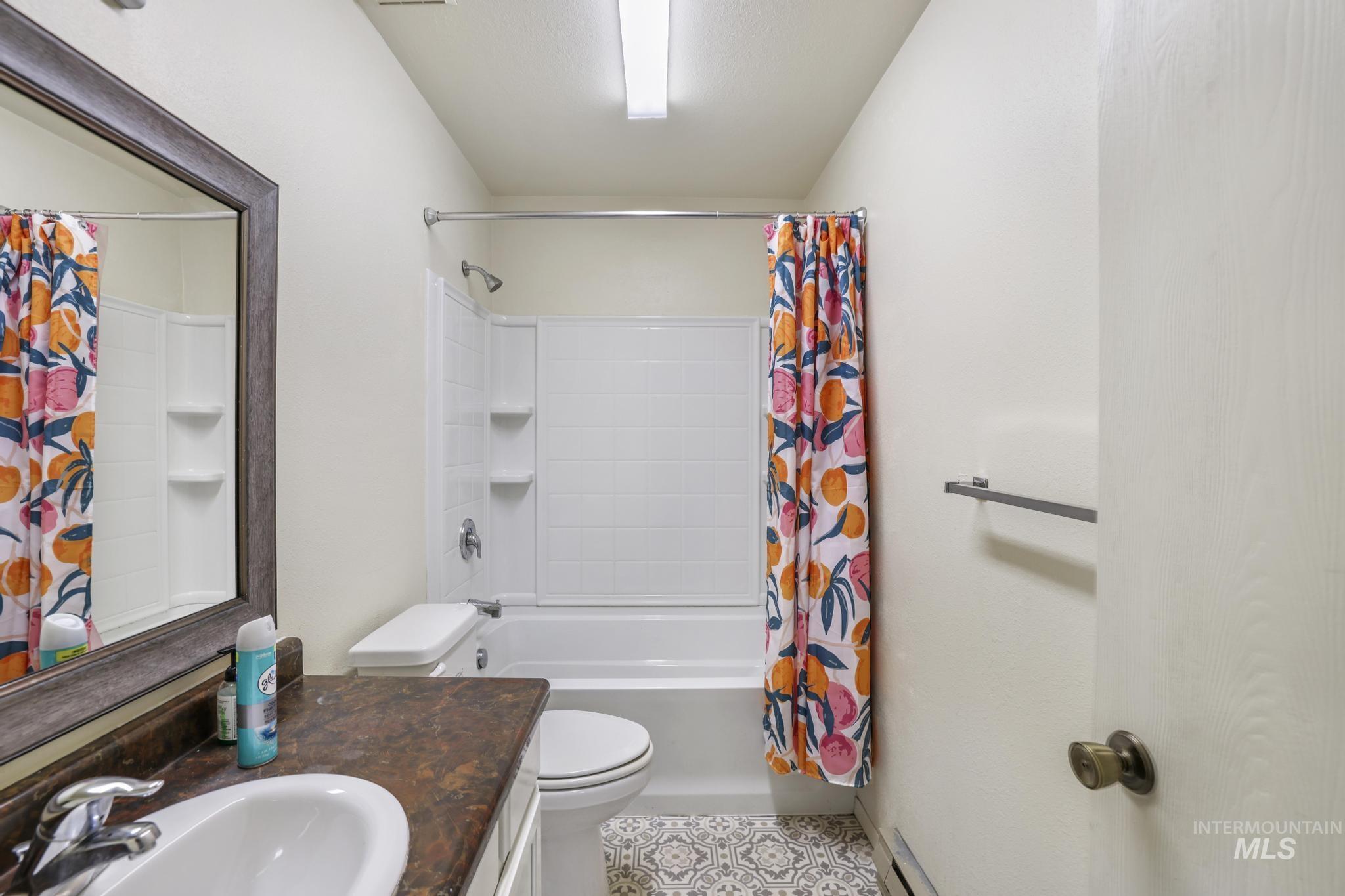 Full bathroom with shower / bath combo with shower curtain, vanity, light tile patterned floors, and baseboard heating
