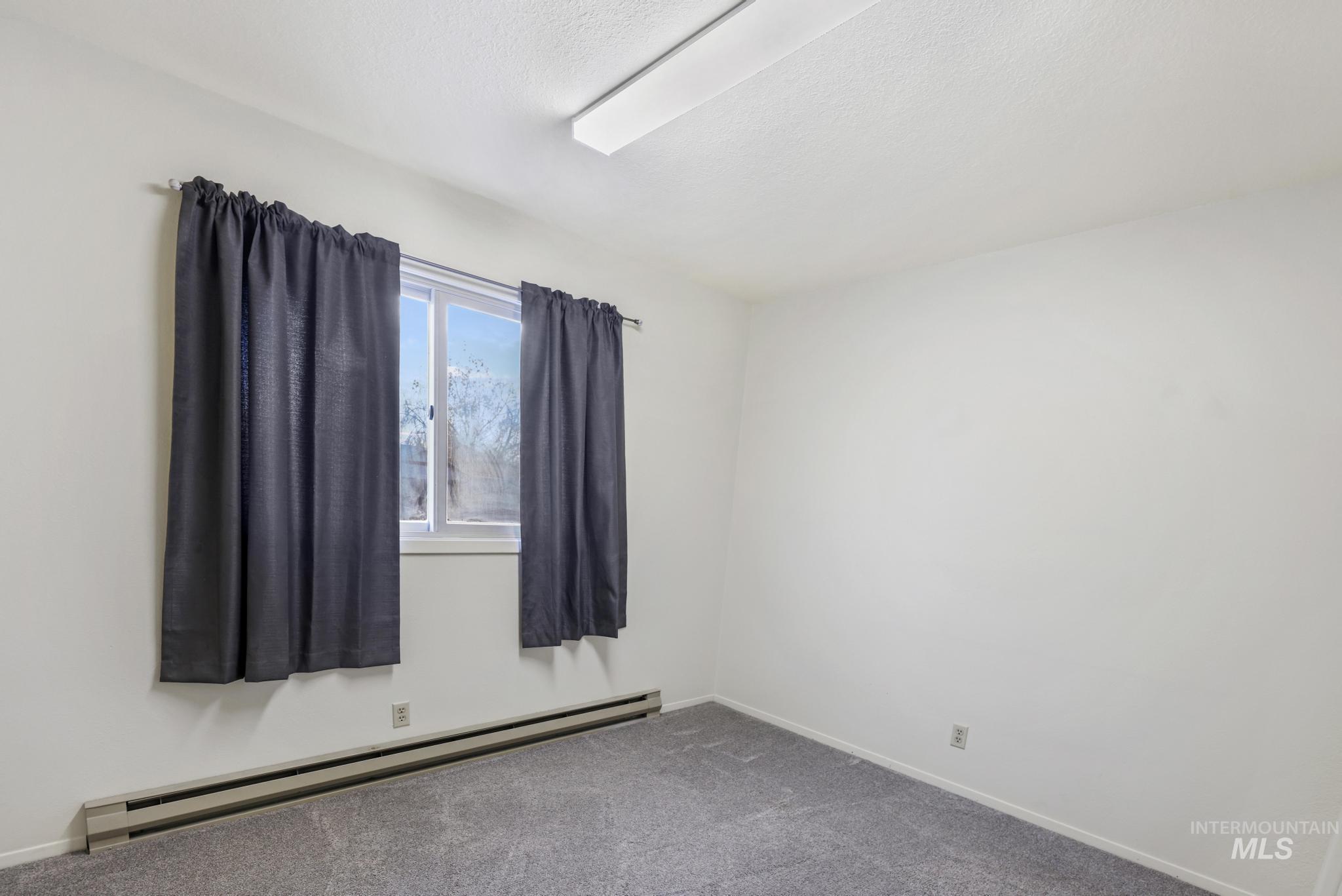 Spare room with a baseboard radiator, carpet, and a textured ceiling