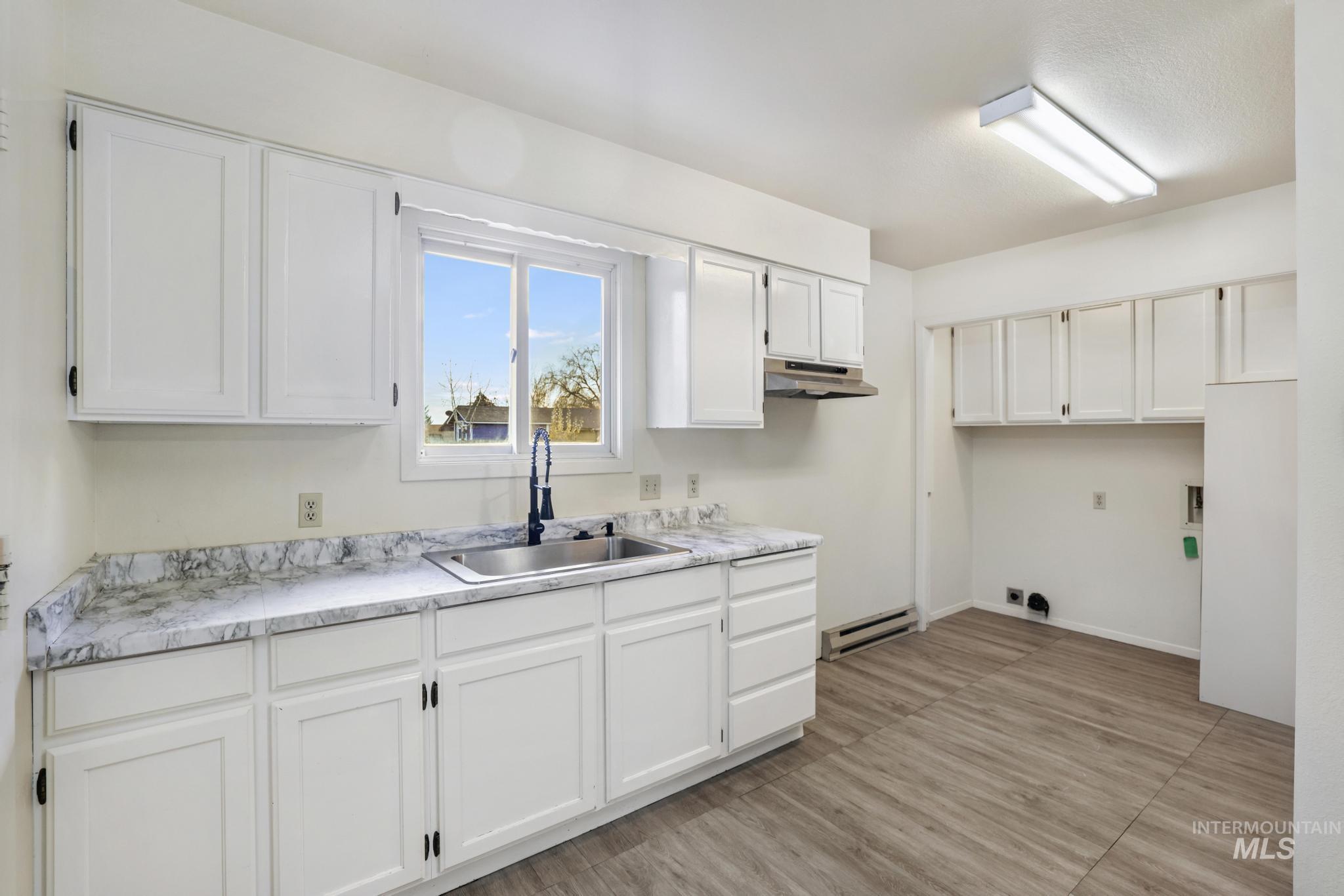 Kitchen with white cabinets, light countertops, light wood-style floors, a baseboard heating unit, and under cabinet range hood