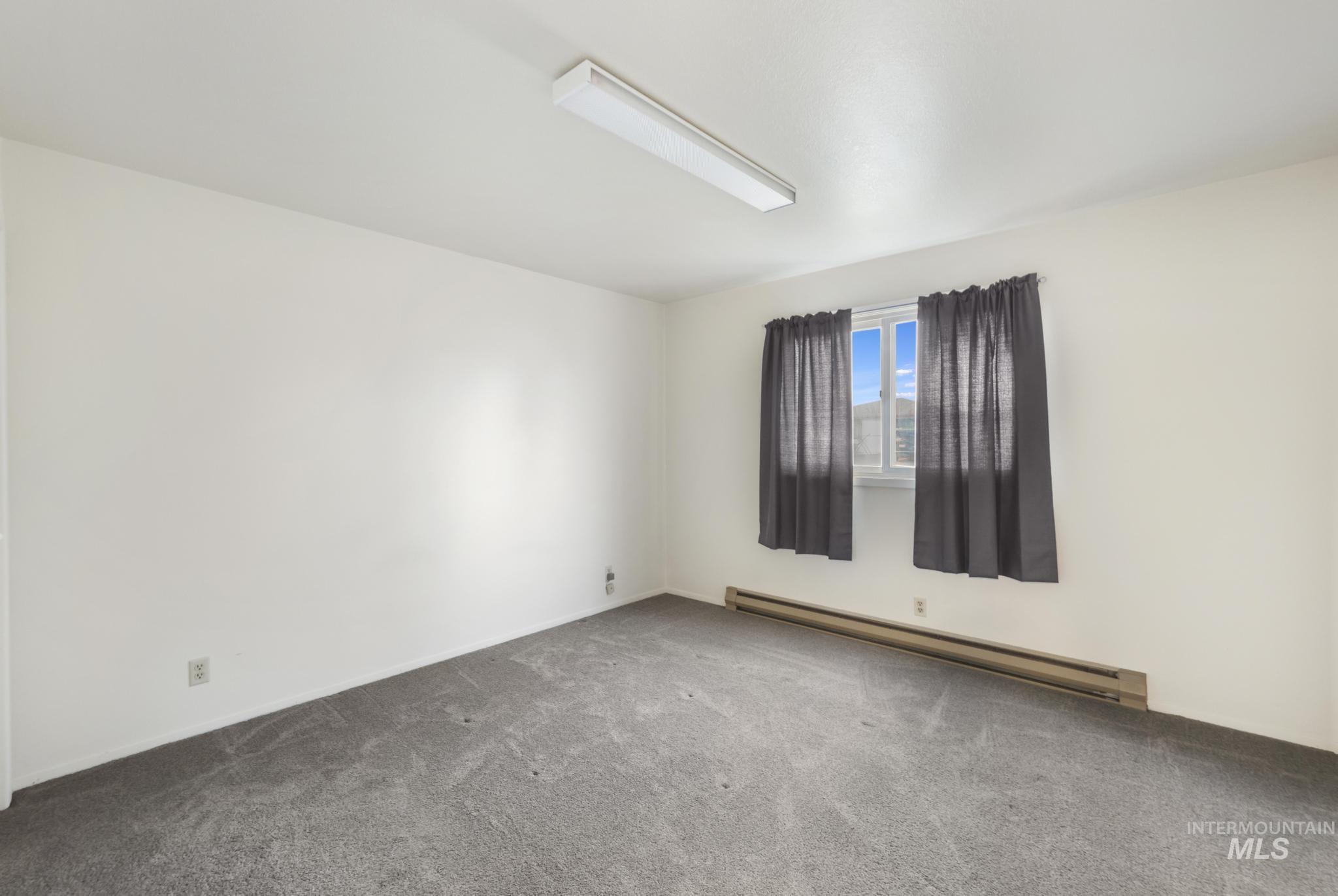 Empty room with a baseboard heating unit and carpet floors