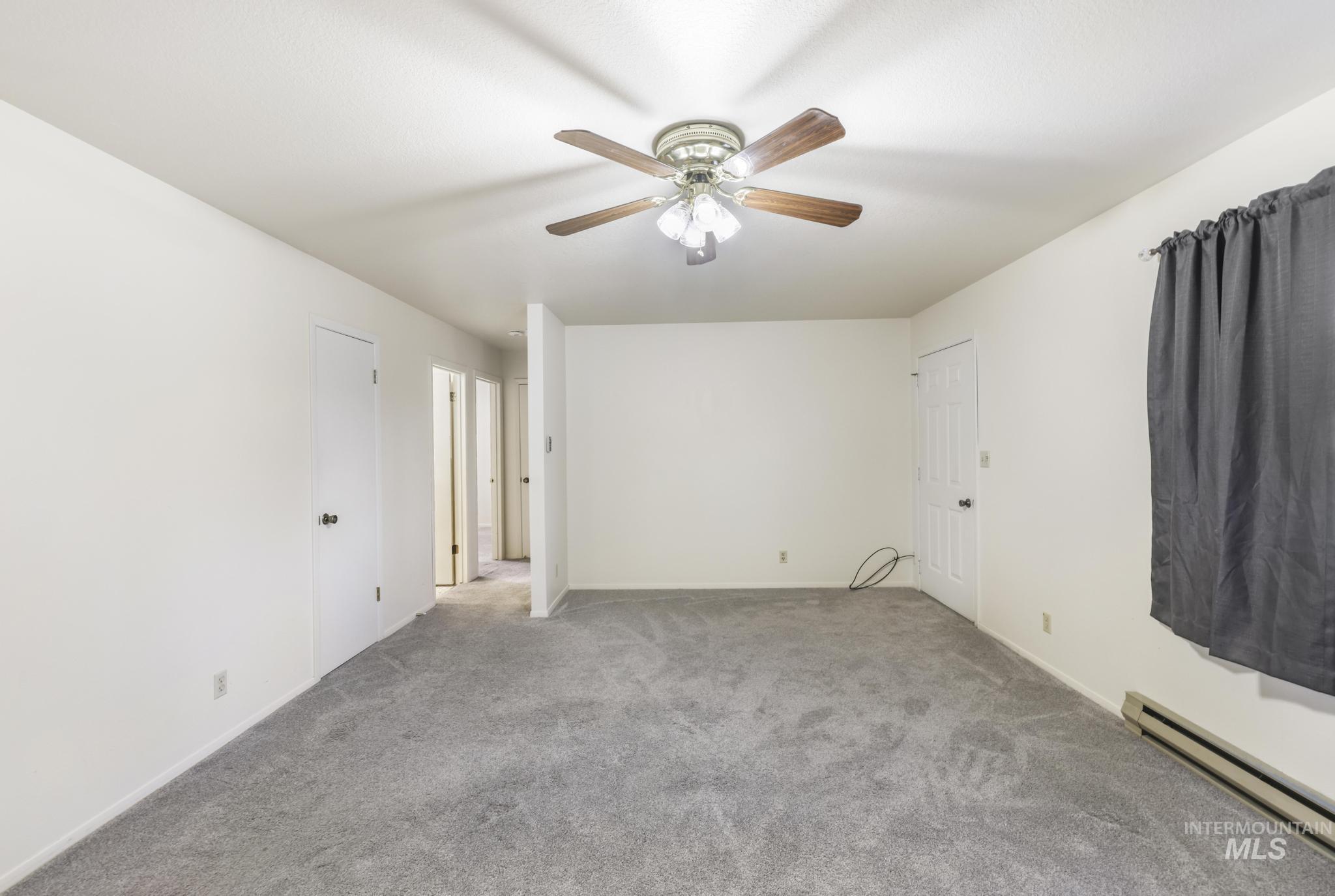 Carpeted spare room featuring a baseboard heating unit and a ceiling fan