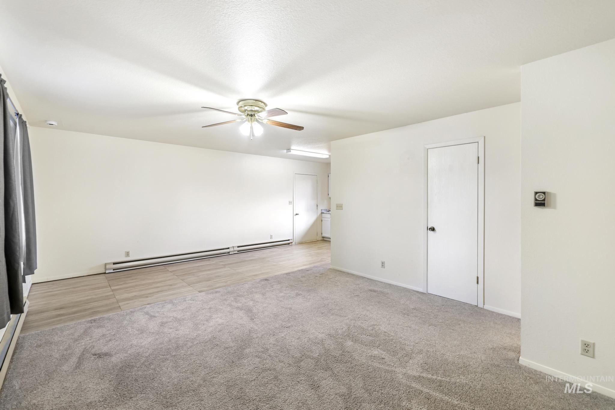 Empty room with light carpet, baseboard heating, and ceiling fan