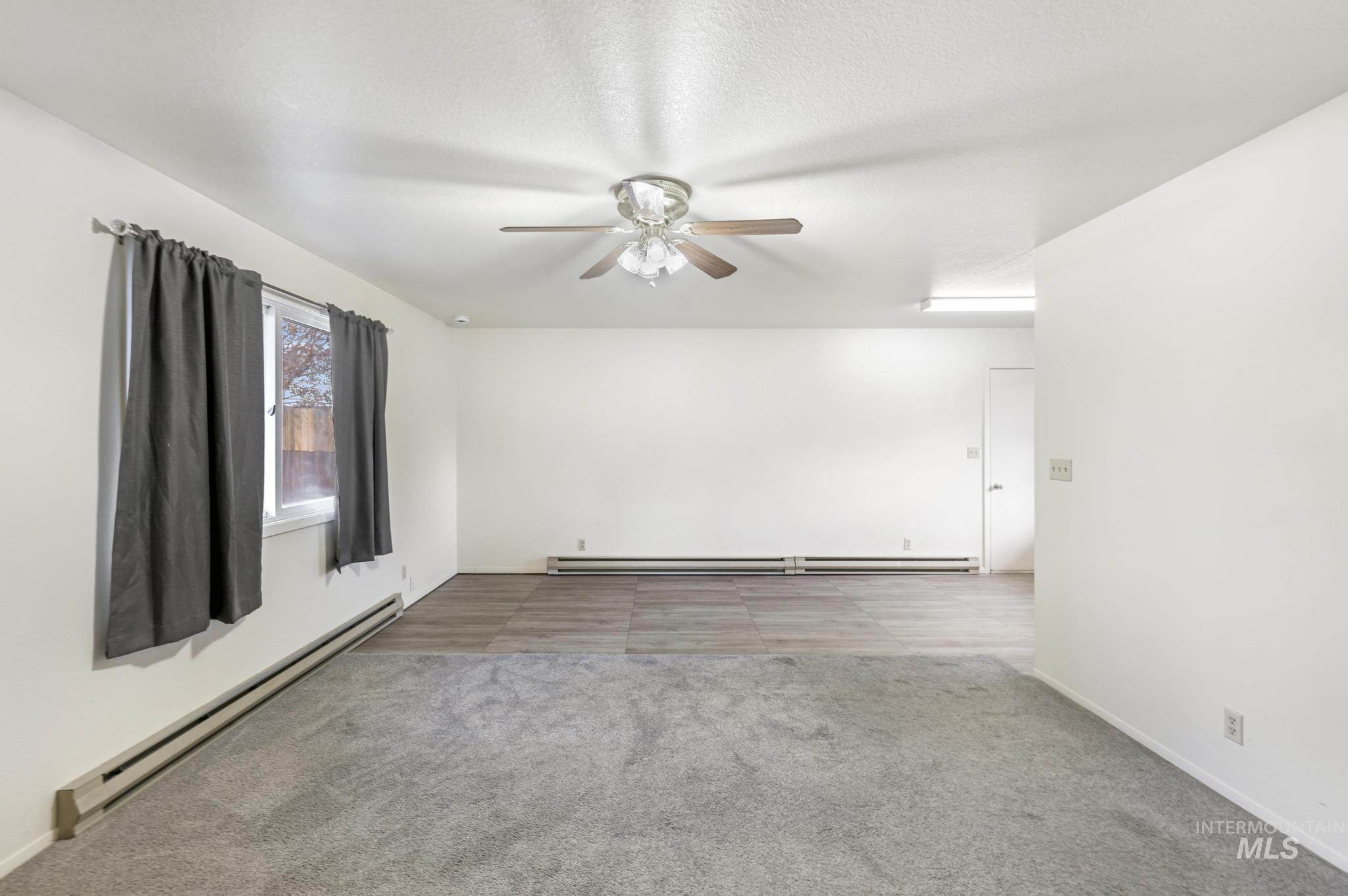 Empty room featuring baseboard heating, light carpet, and a ceiling fan