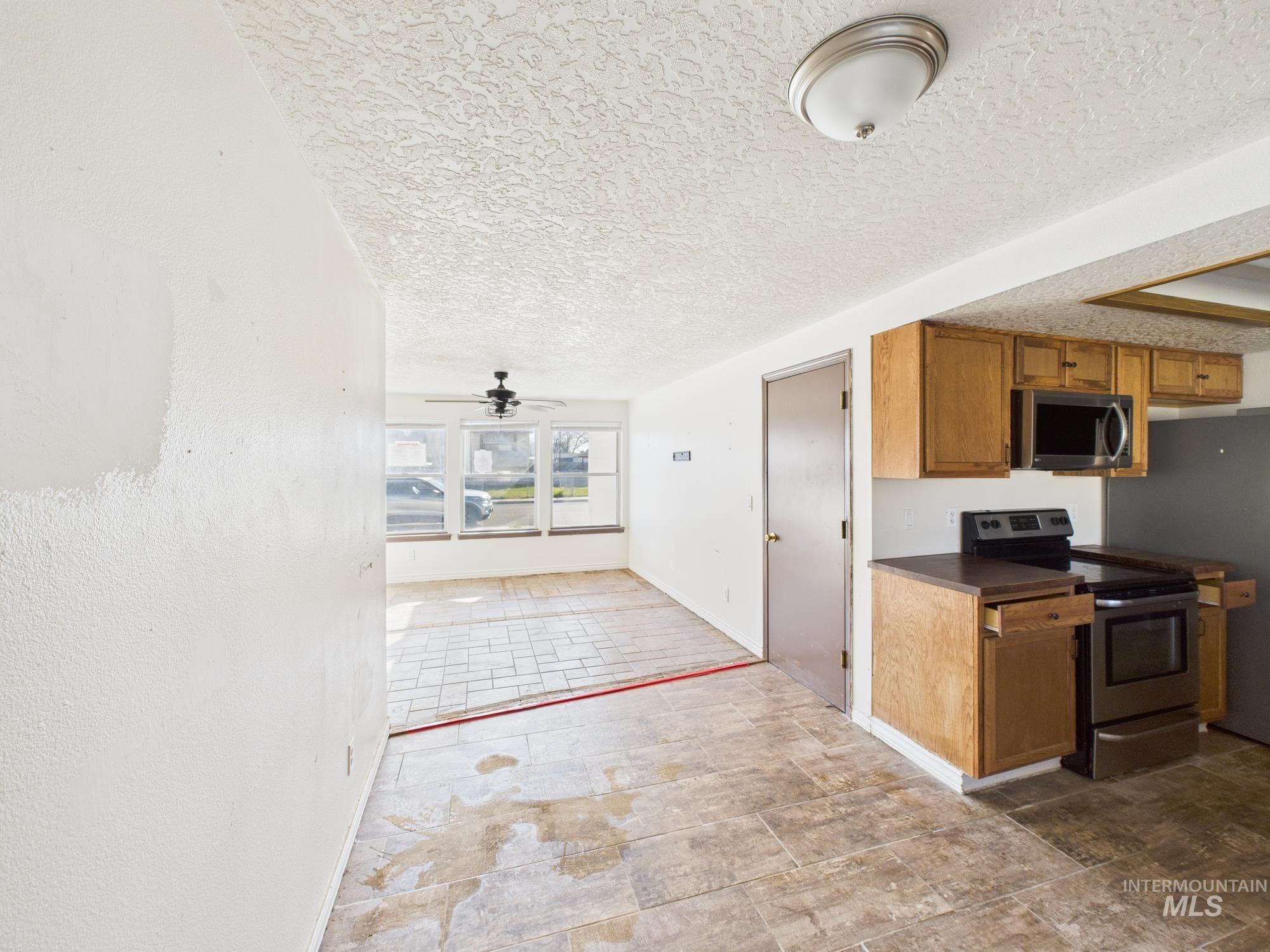 Kitchen featuring stainless steel appliances, brown cabinetry, dark countertops, a textured ceiling, and a ceiling fan