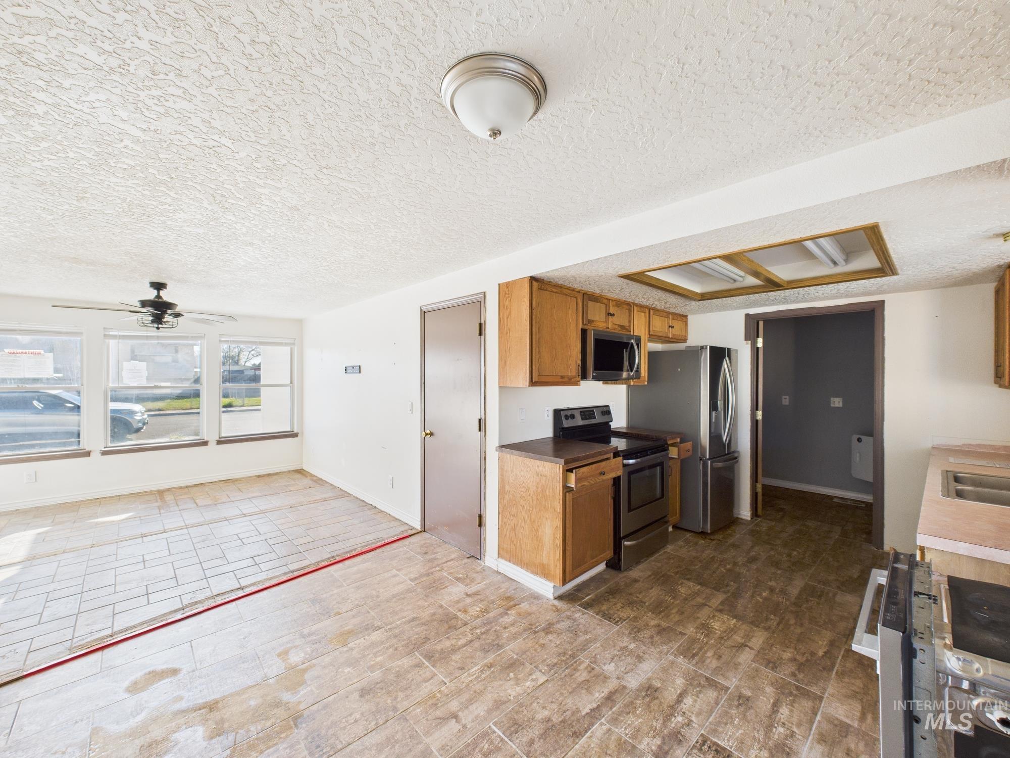 Kitchen with appliances with stainless steel finishes, ceiling fan, a textured ceiling, brown cabinets, and dark countertops
