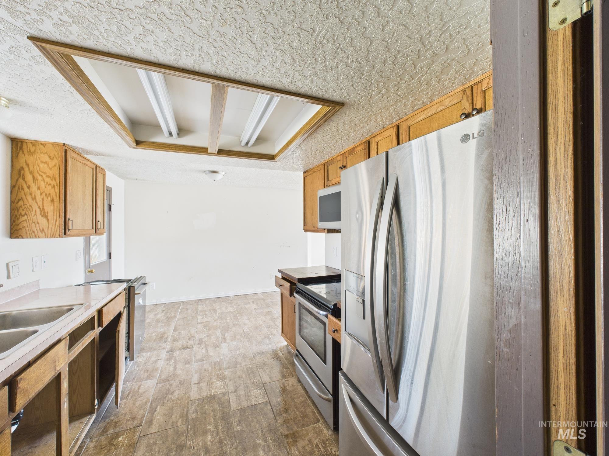 Kitchen featuring a textured ceiling, appliances with stainless steel finishes, light countertops, and brown cabinetry