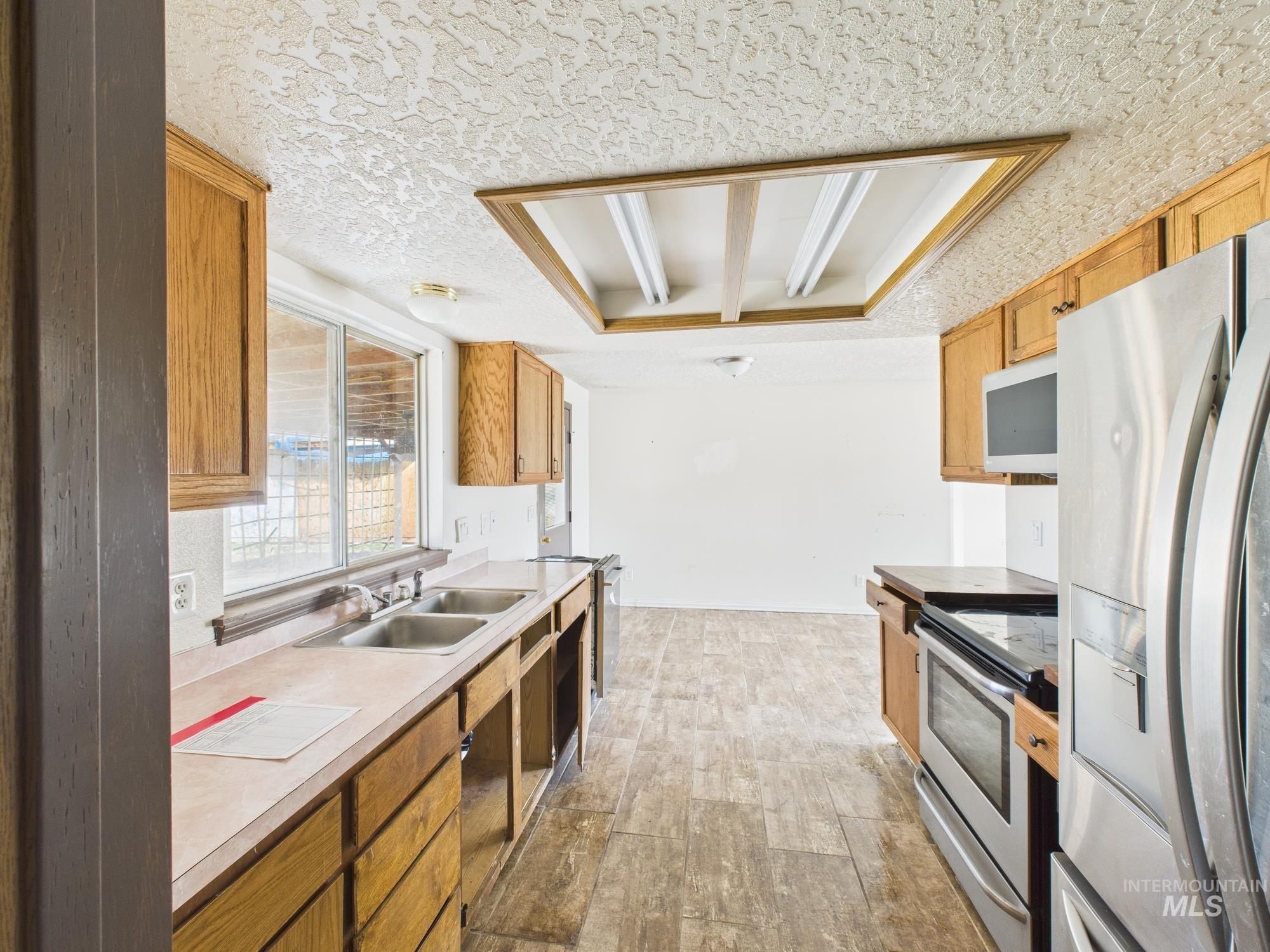 Kitchen featuring appliances with stainless steel finishes, a textured ceiling, light countertops, light wood-style flooring, and brown cabinets