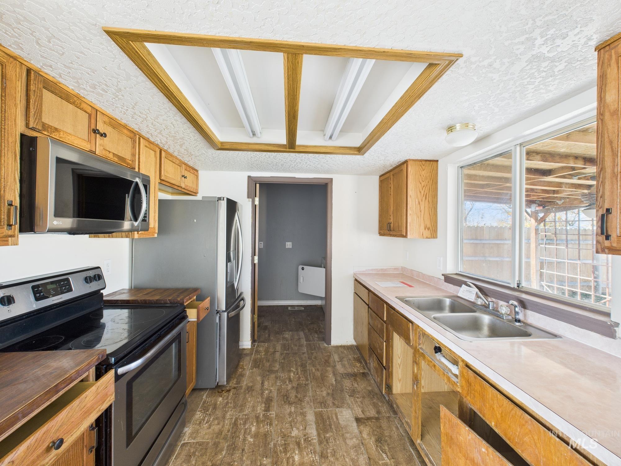Kitchen with appliances with stainless steel finishes, dark wood finished floors, a textured ceiling, light countertops, and brown cabinets