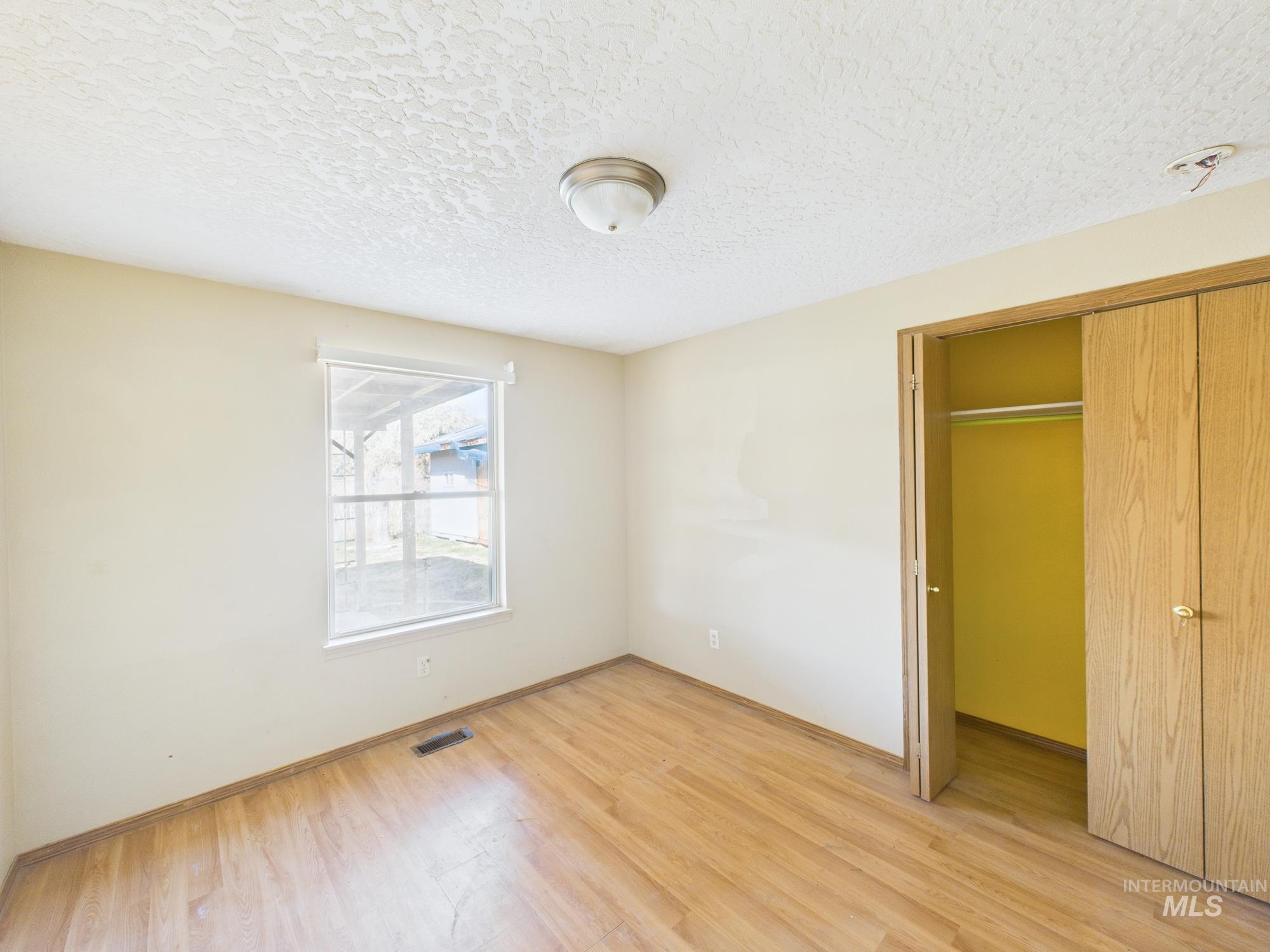 Unfurnished bedroom featuring light wood-style floors, a textured ceiling, and a closet