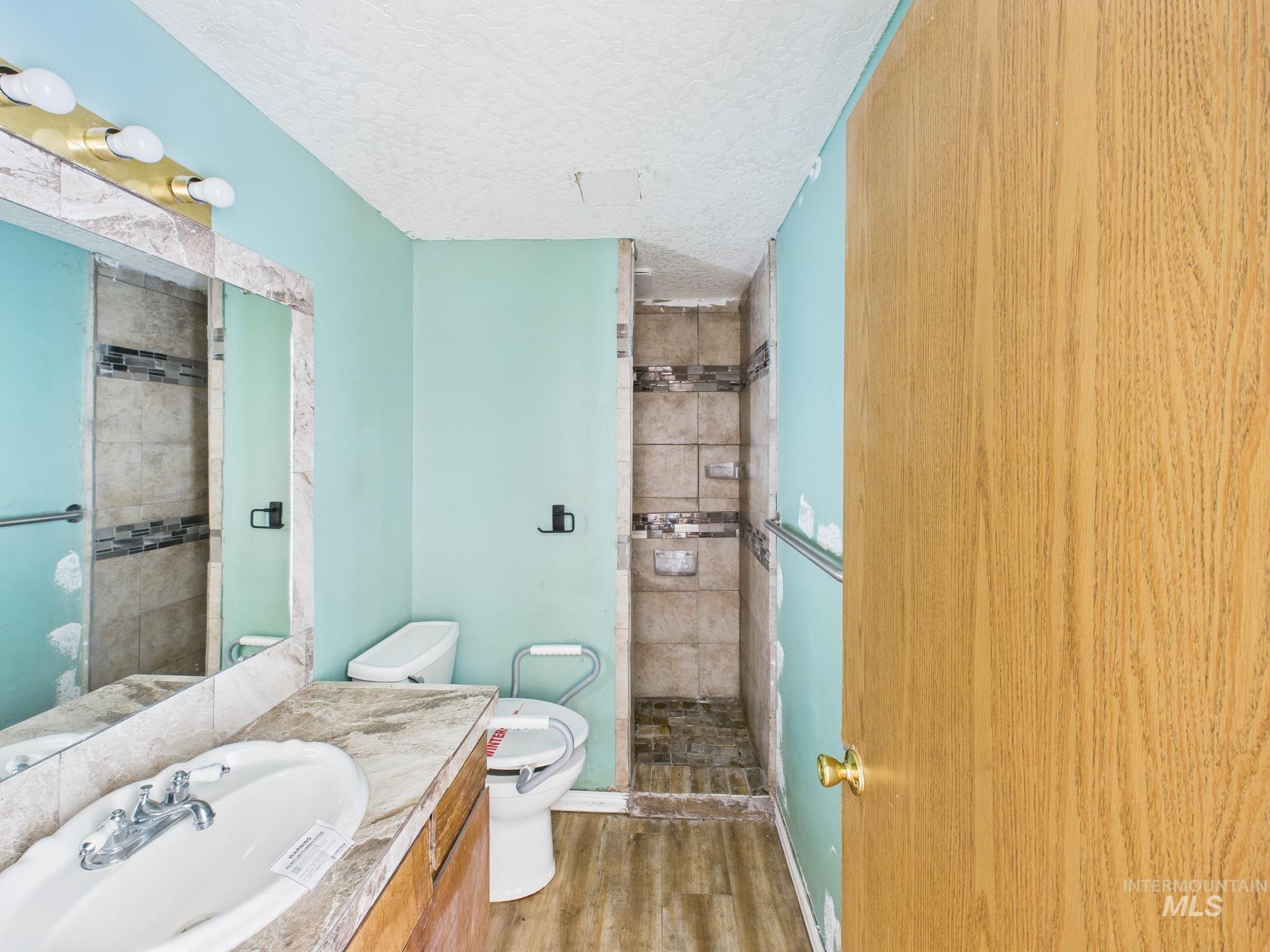 Full bathroom with a textured ceiling, wood finished floors, a shower stall, and vanity